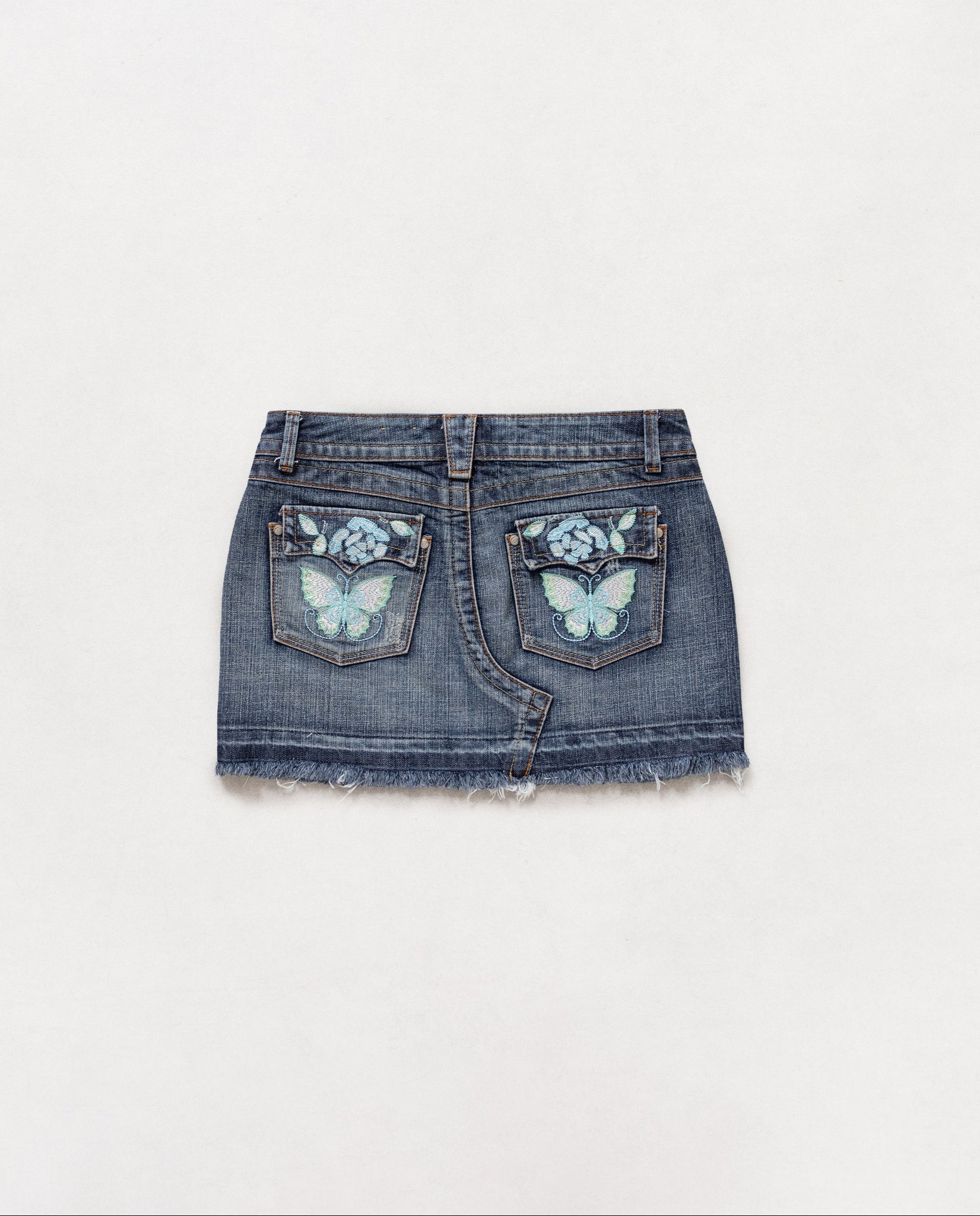 A vintage 2000's low rise denim mini skirt with embroidered butterflies on the back pockets, displayed against a white background.