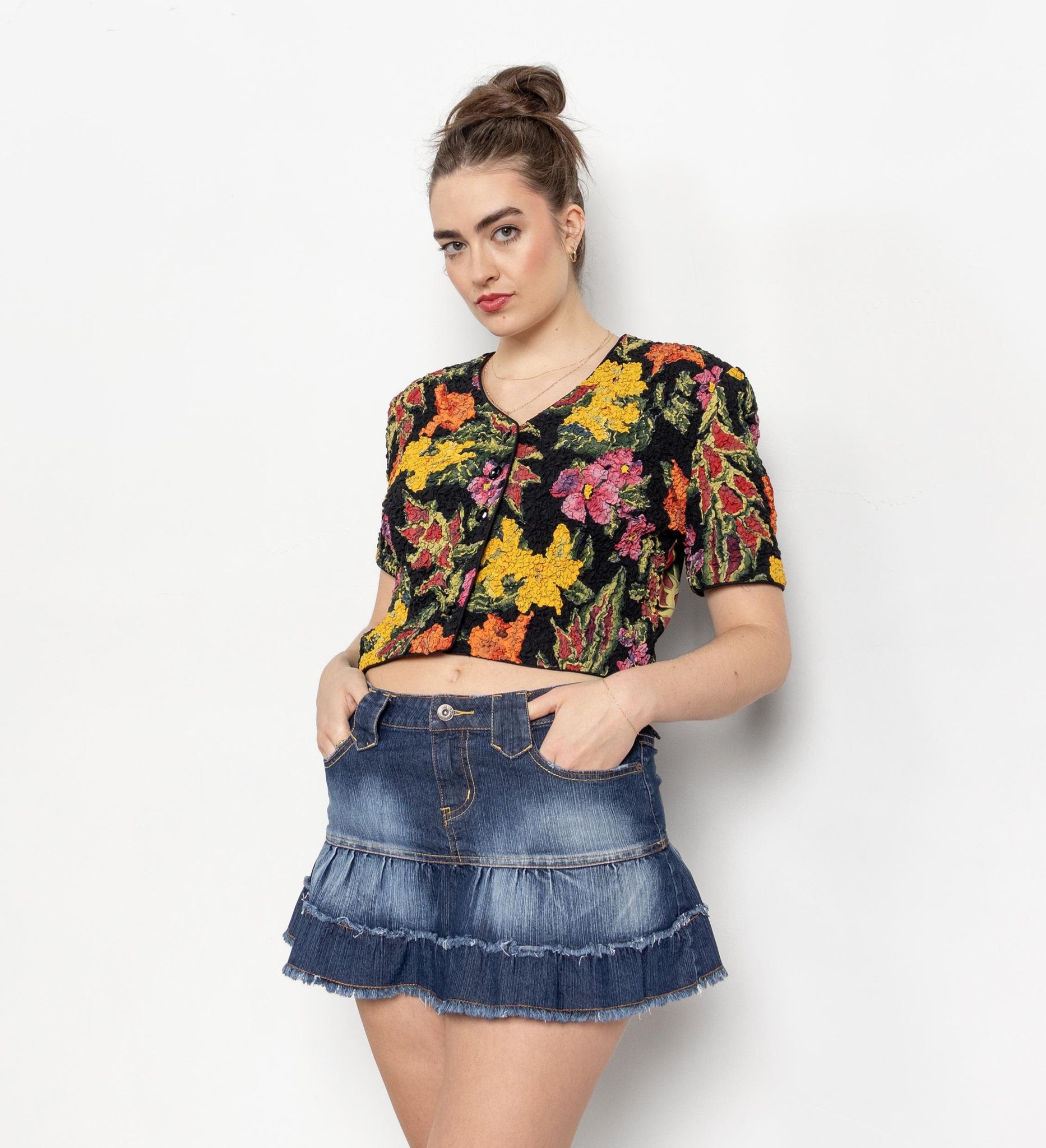 Woman wearing a colorful floral top and denim skirt on a white background