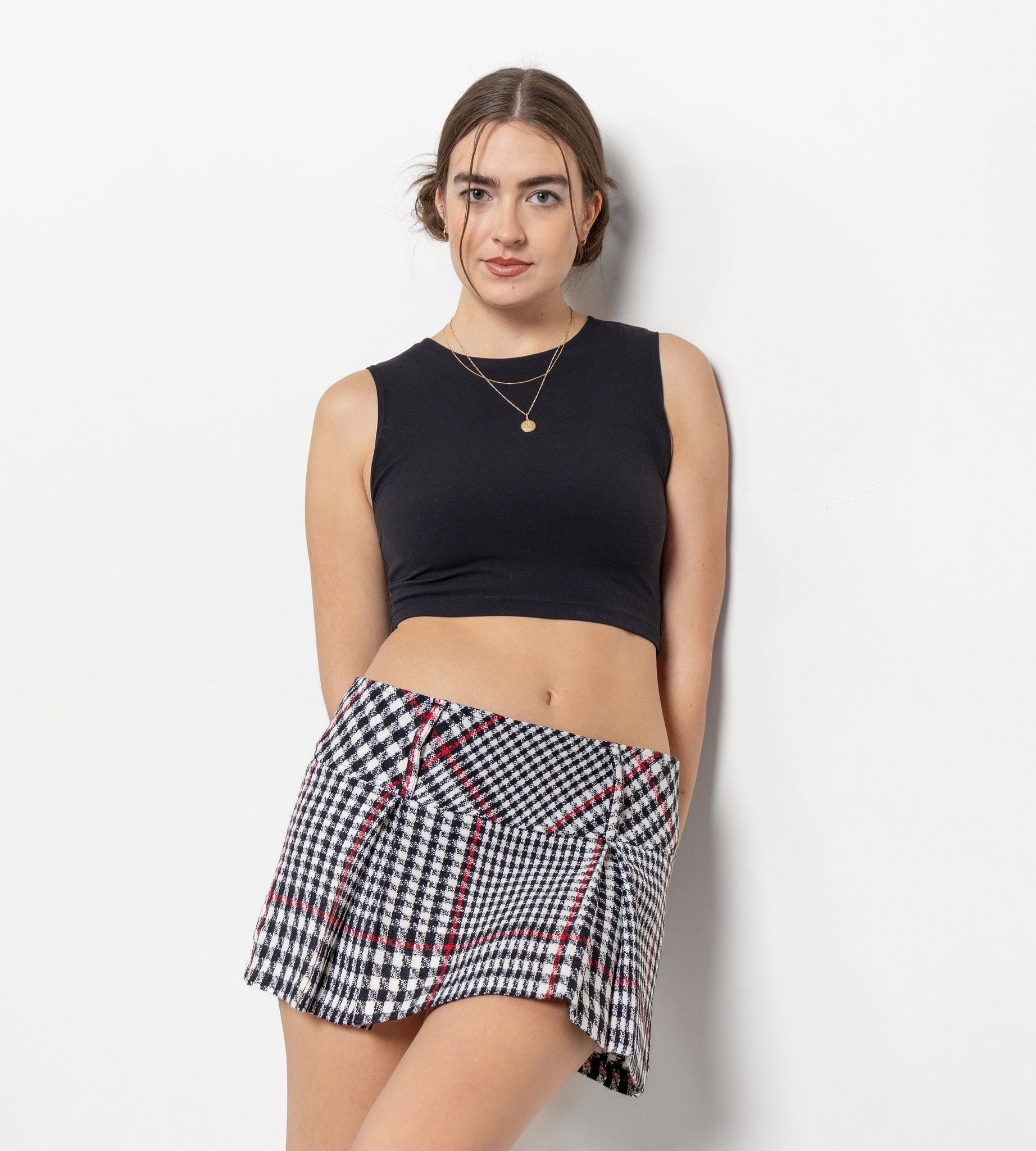 Woman wearing a black sleeveless top and plaid skirt on a white background