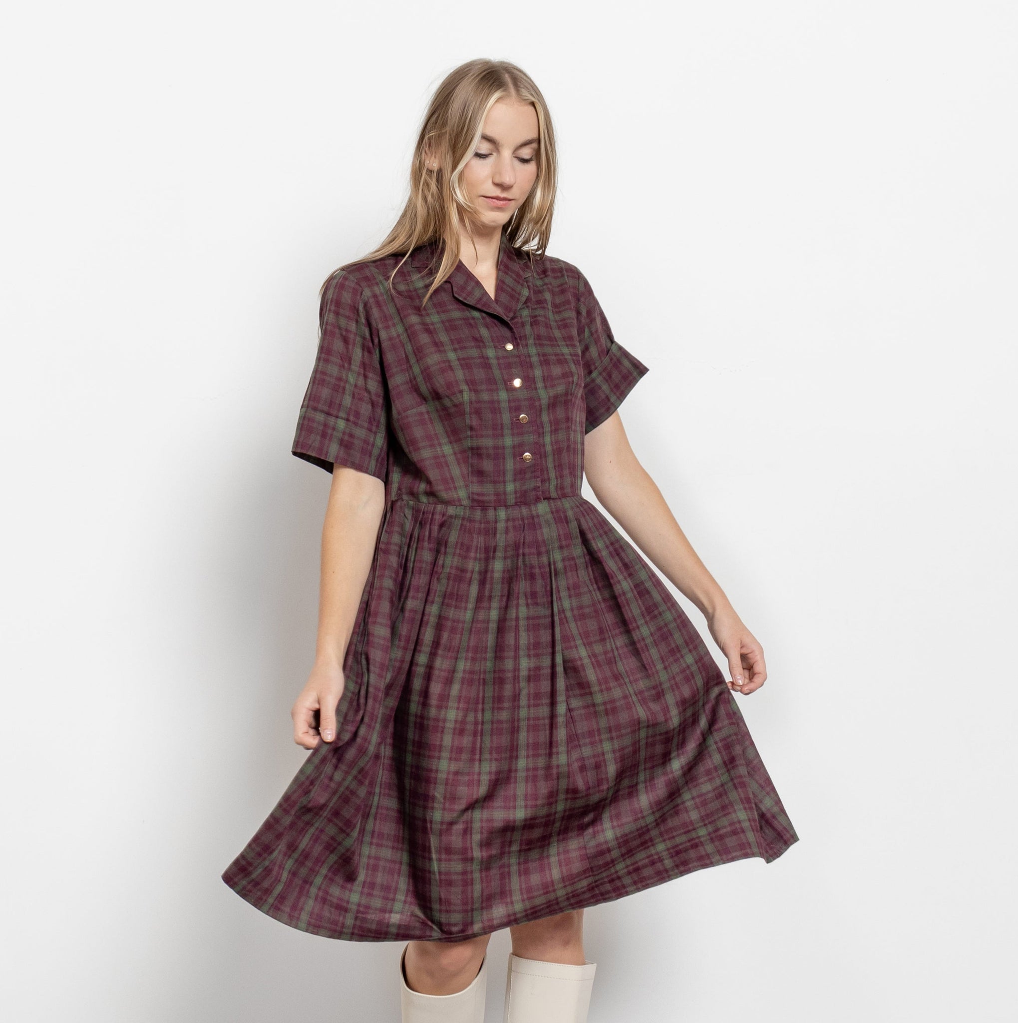 A woman modeling a vintage 90's plaid midi short sleeve house dress with buttons down the front bodice and pleated at the waistline.