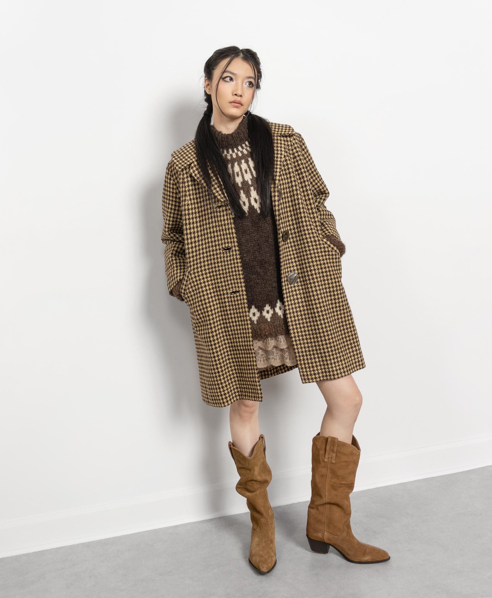 Woman wearing a plaid coat, patterned sweater, and brown boots on a white background