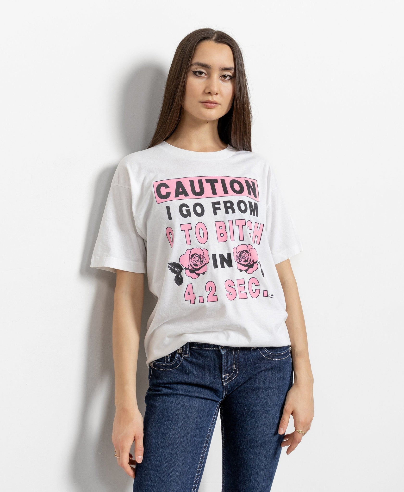 A woman wearing a white crew neck t-shirt with text and a rose graphic on it, paired with blue jeans.