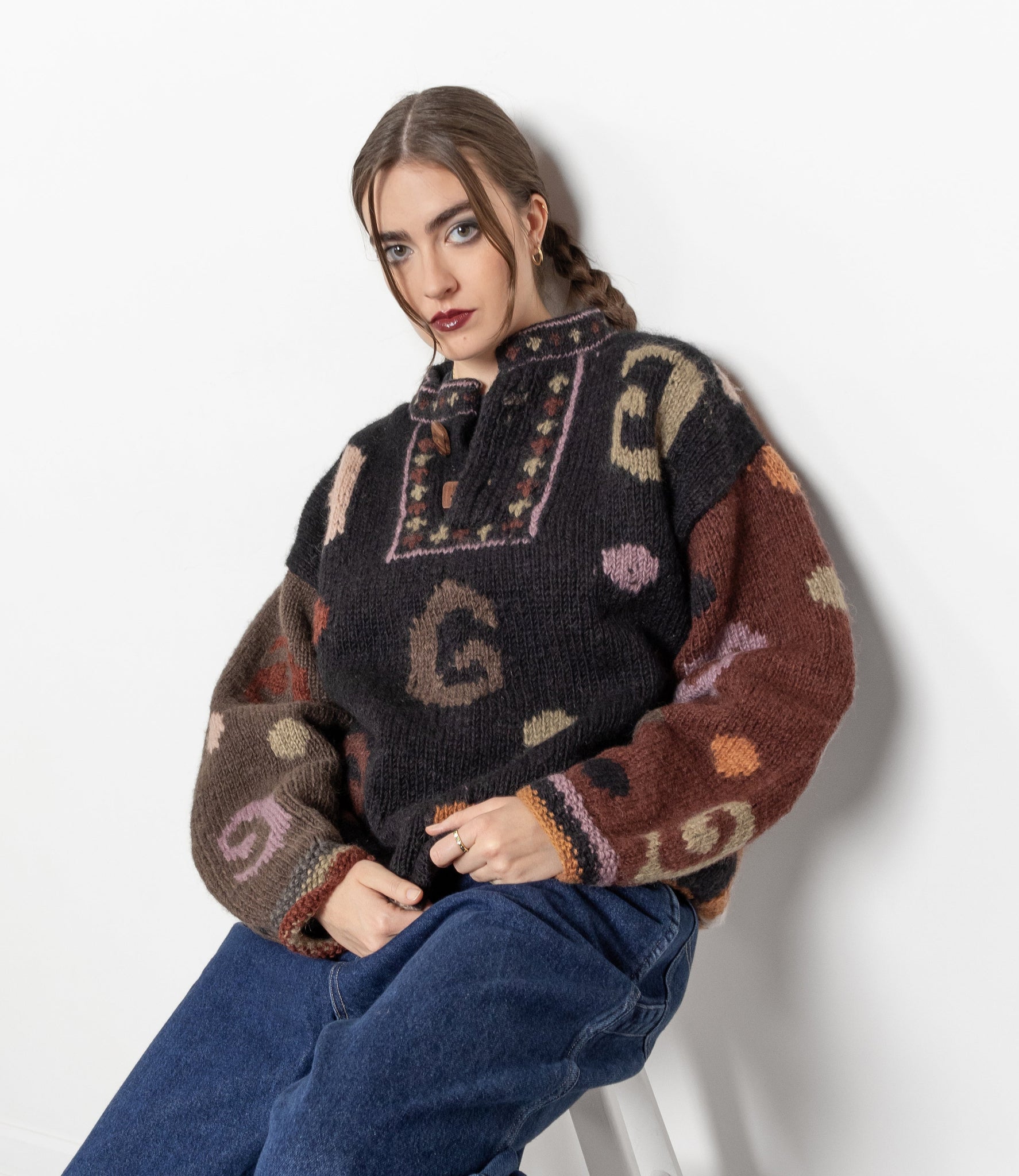 Woman wearing a patterned sweater sitting on a white stool against a white background