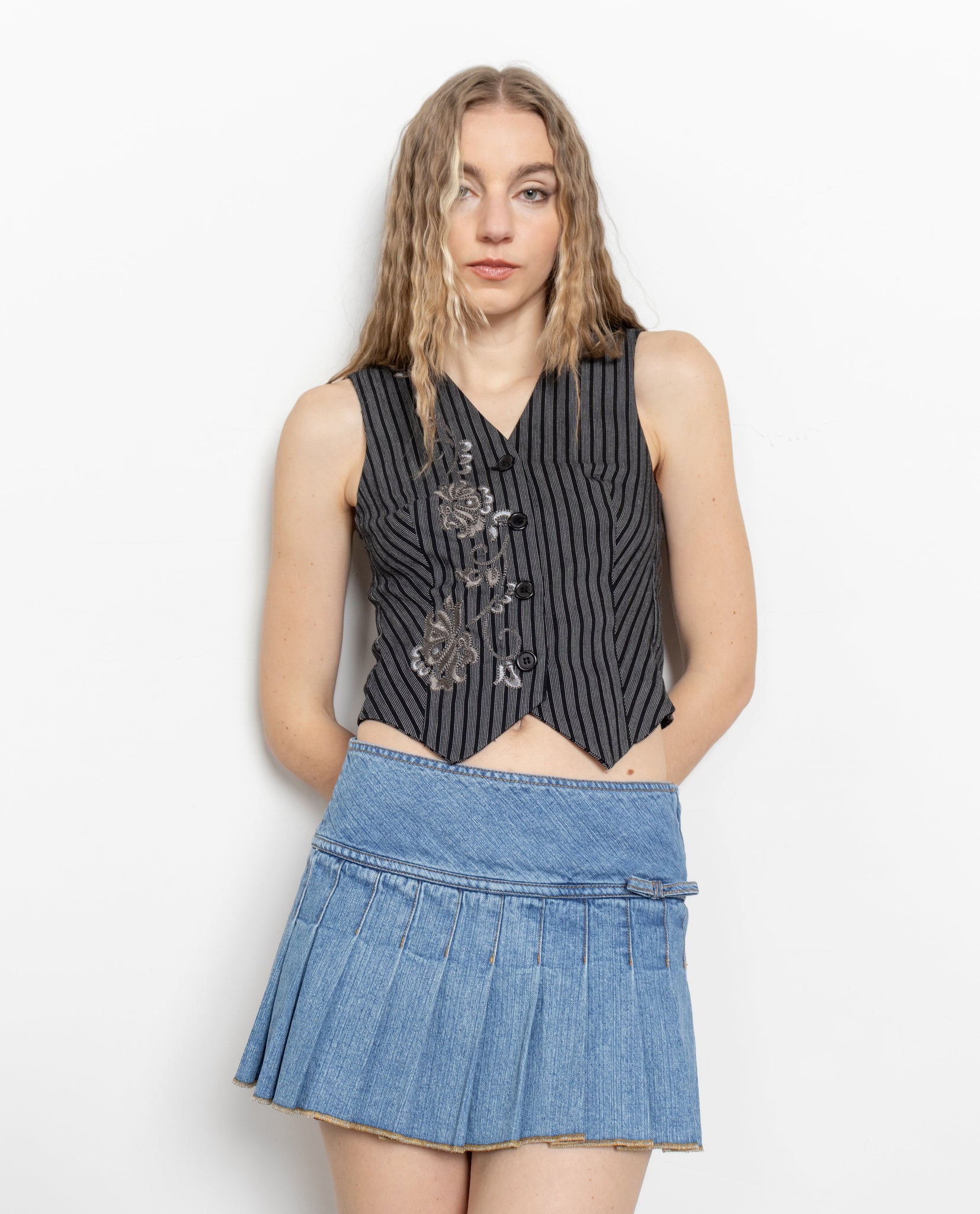 Woman wearing a black sleeveless top with floral embroidery and a blue denim skirt on a white background