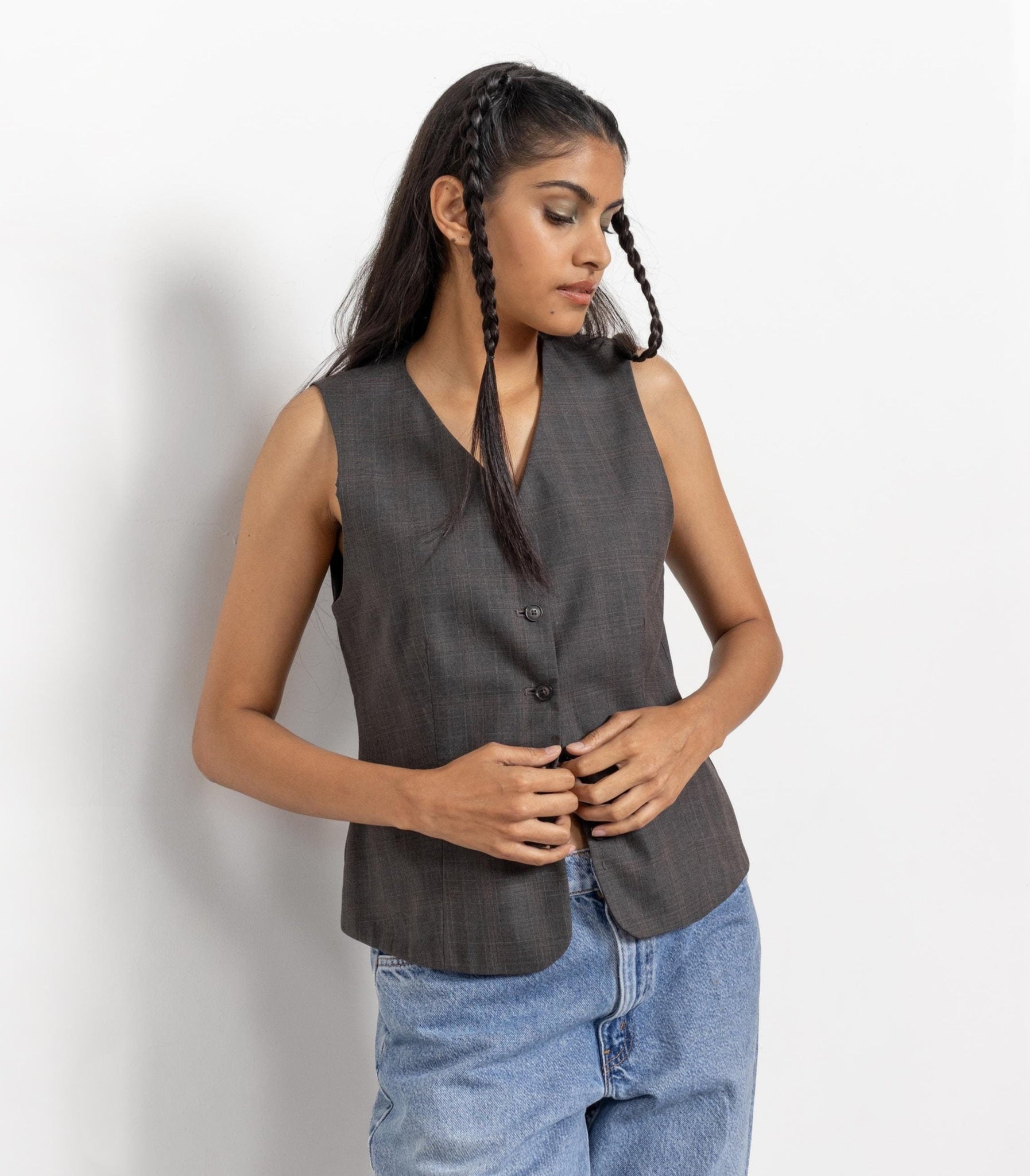 Woman wearing a sleeveless gray top and blue jeans against a white background