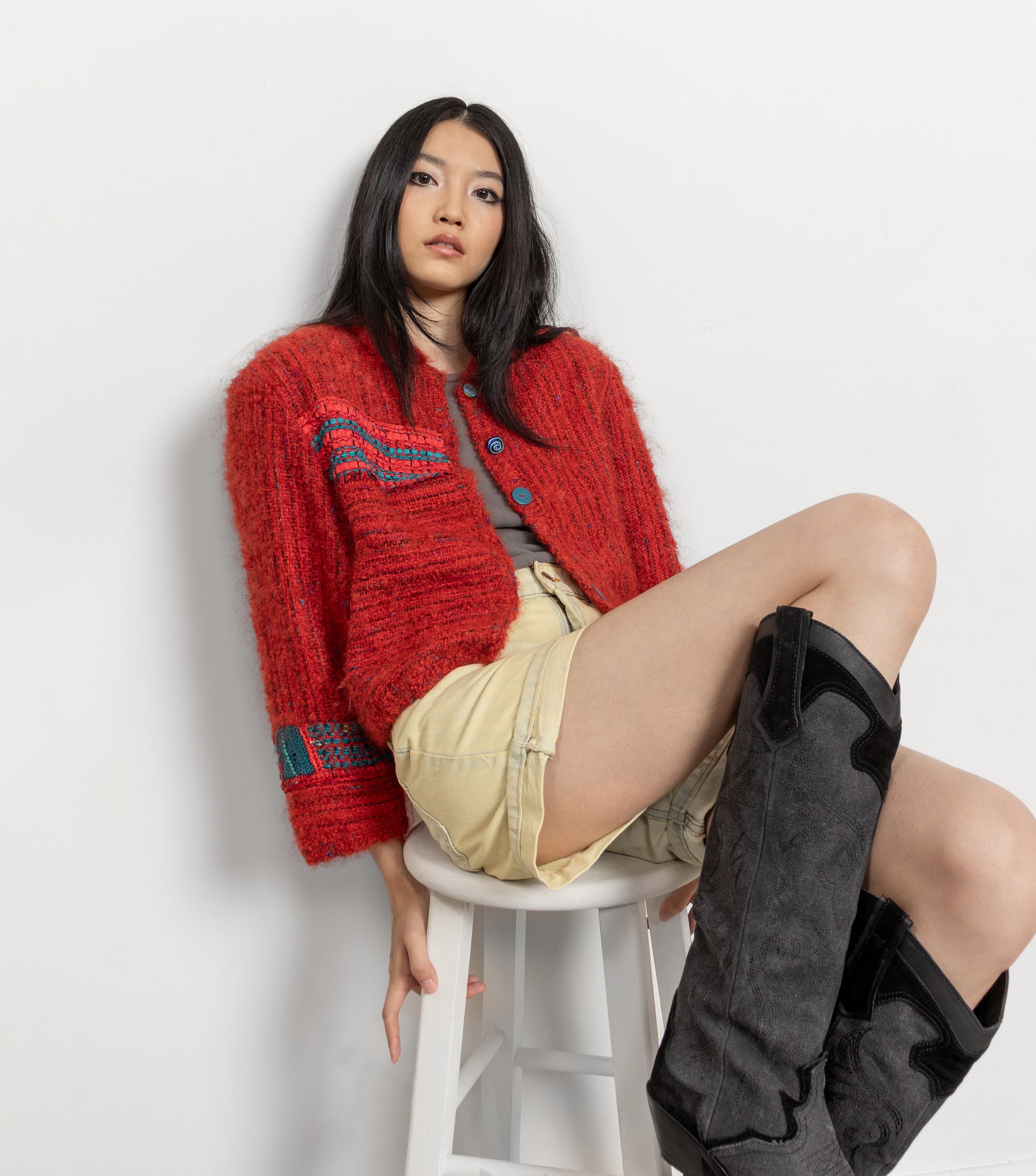 Woman wearing a red cardigan, beige shorts, and black knee-high boots on a white background