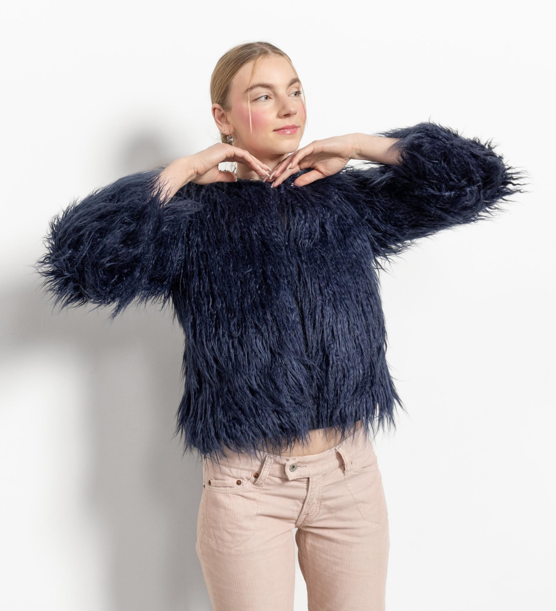 A person modeling a navy blue faux mongolian fur jacket with long sleeves and side pockets.