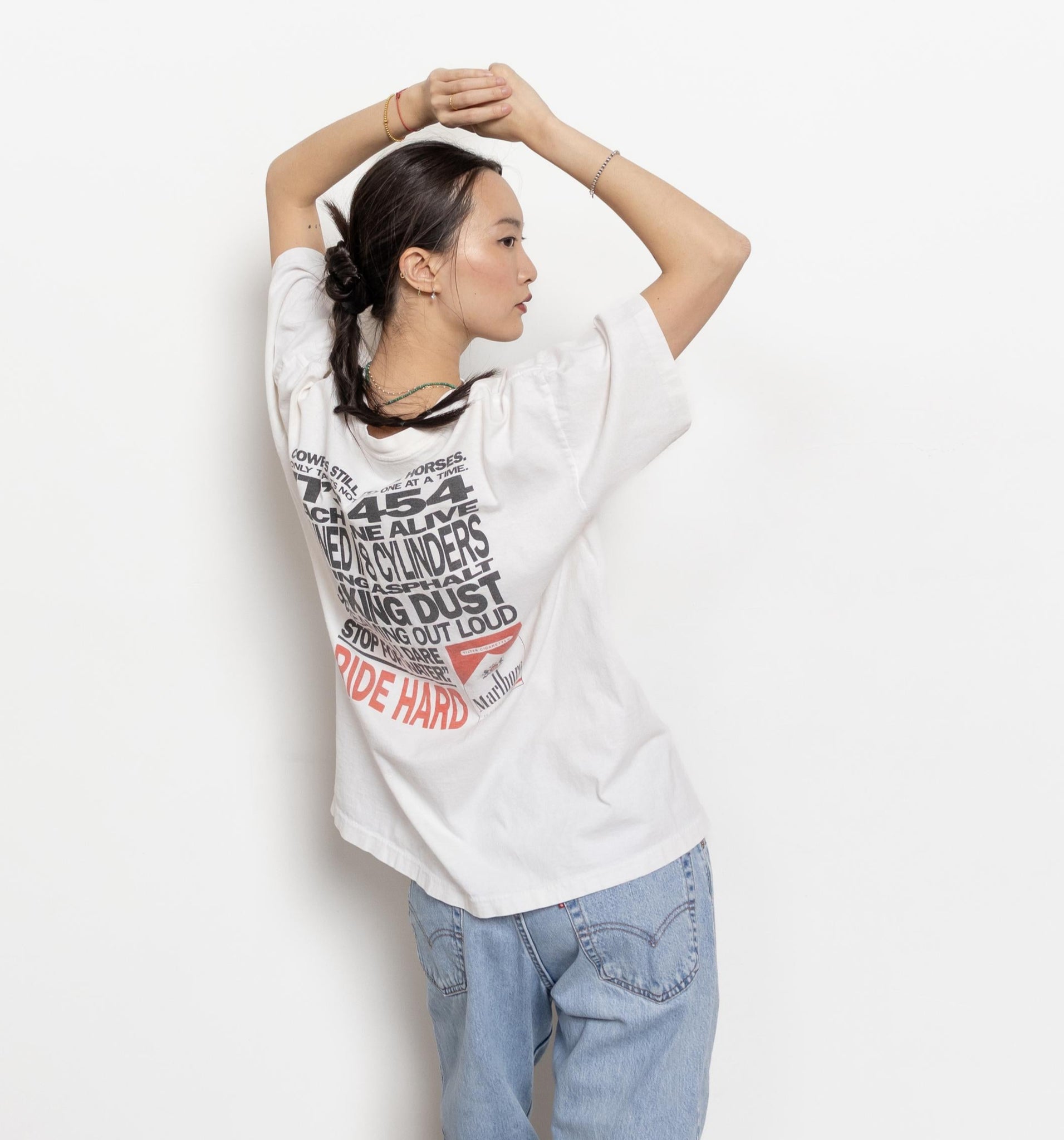 A person standing with their hands raised wearing a white Marlboro cigarette t-shirt with a large graphic on the back, in front of a white background.