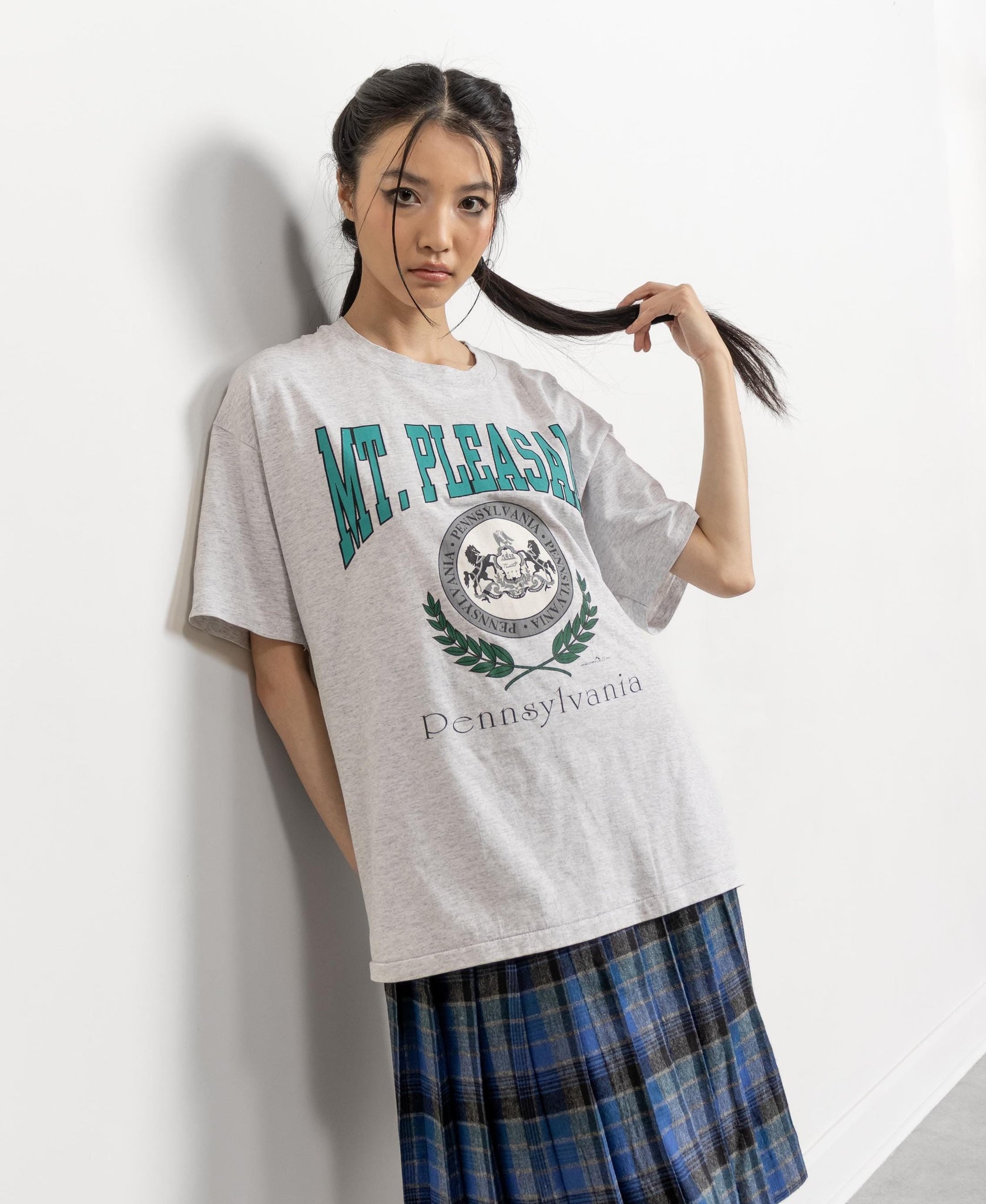 Person wearing a gray t-shirt with 'Mt. Pleasants' text and a plaid skirt on a white background