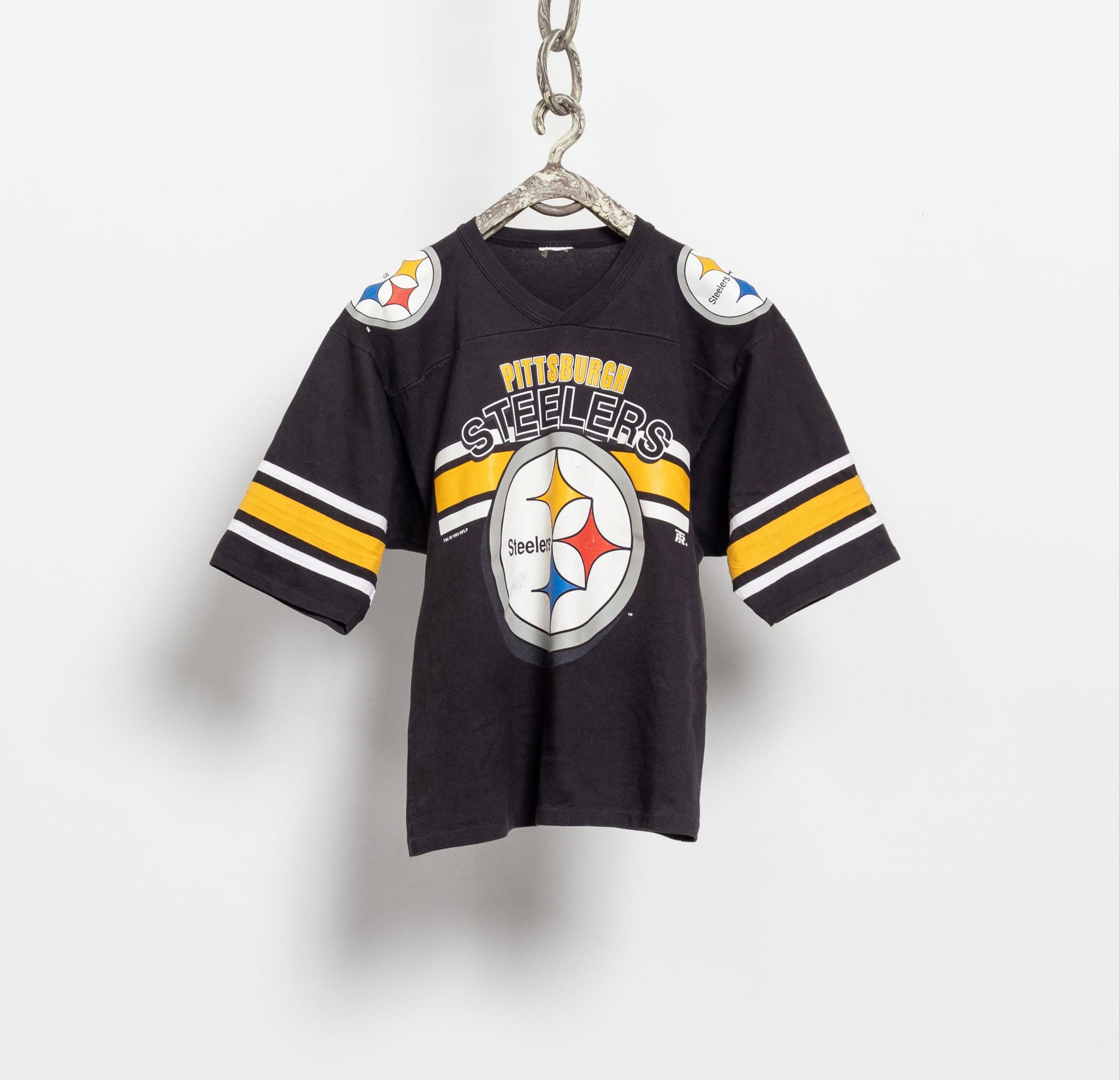 A vintage 90's NFL Pittsburgh Steelers short sleeve black jersey with oversized Steelers lettering and logo on the front, displayed on a hanger.