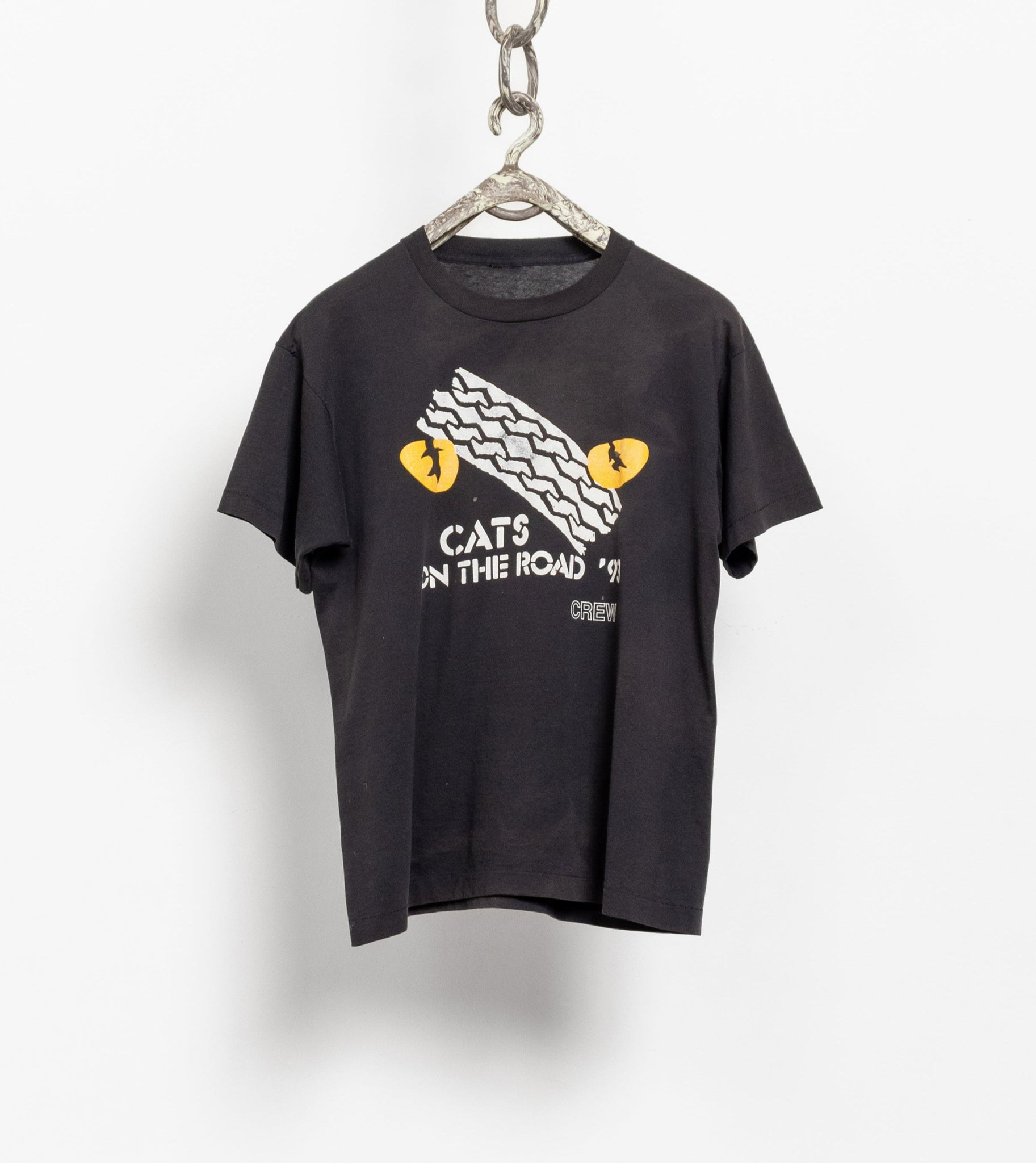 A black t-shirt with the text 'Cats by the Road' printed on the front, hanging on a chain.