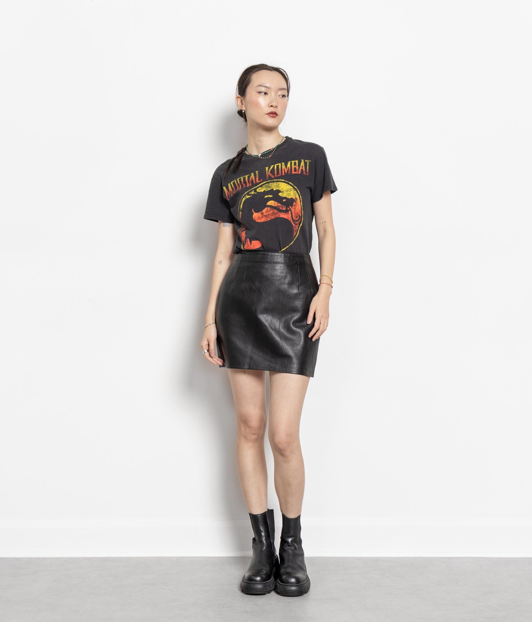 A model wearing a vintage 90's black genuine leather high waisted mini skirt with a graphic t-shirt and black boots.