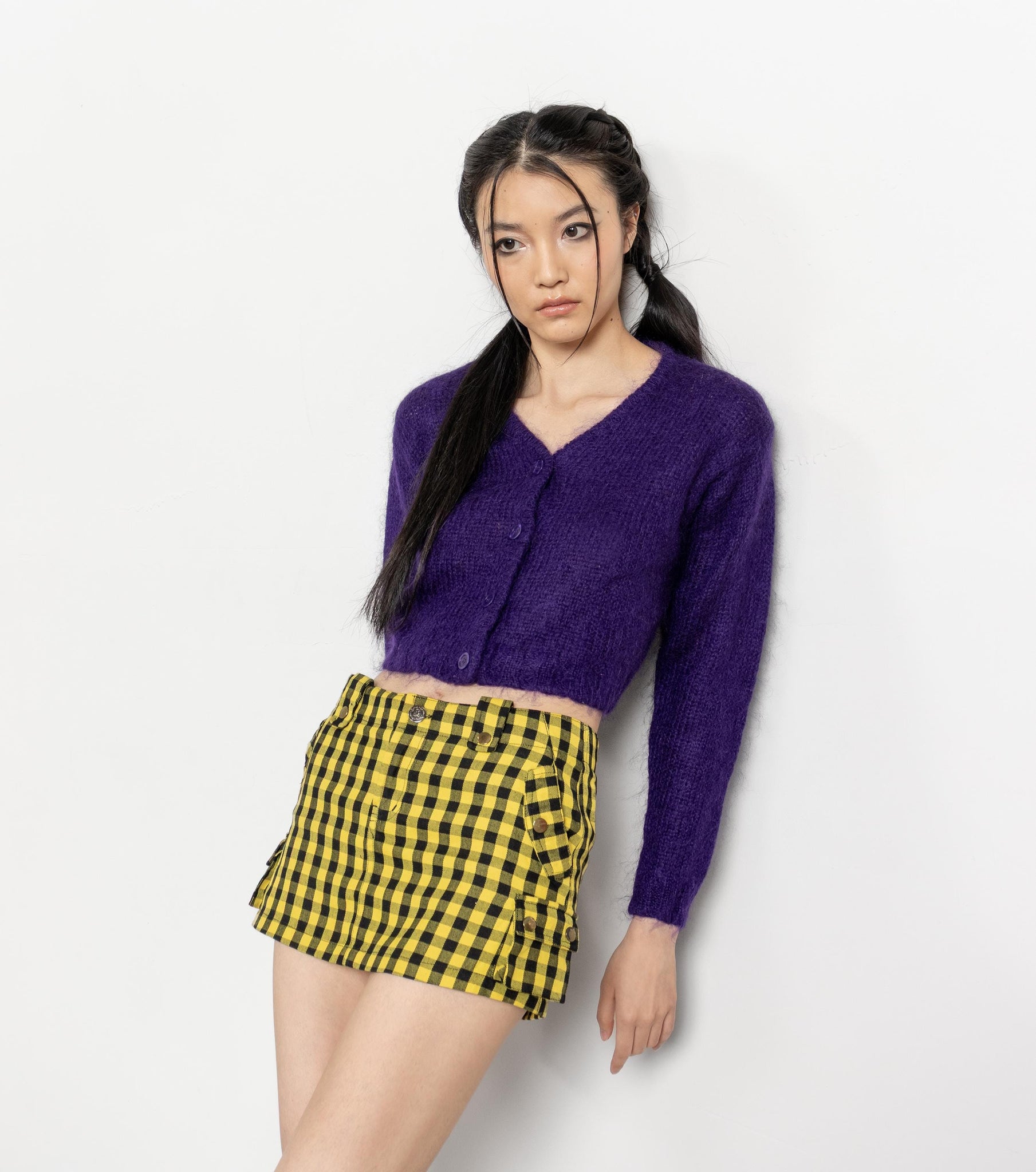 Woman wearing a purple cardigan and yellow checkered skirt against a white background