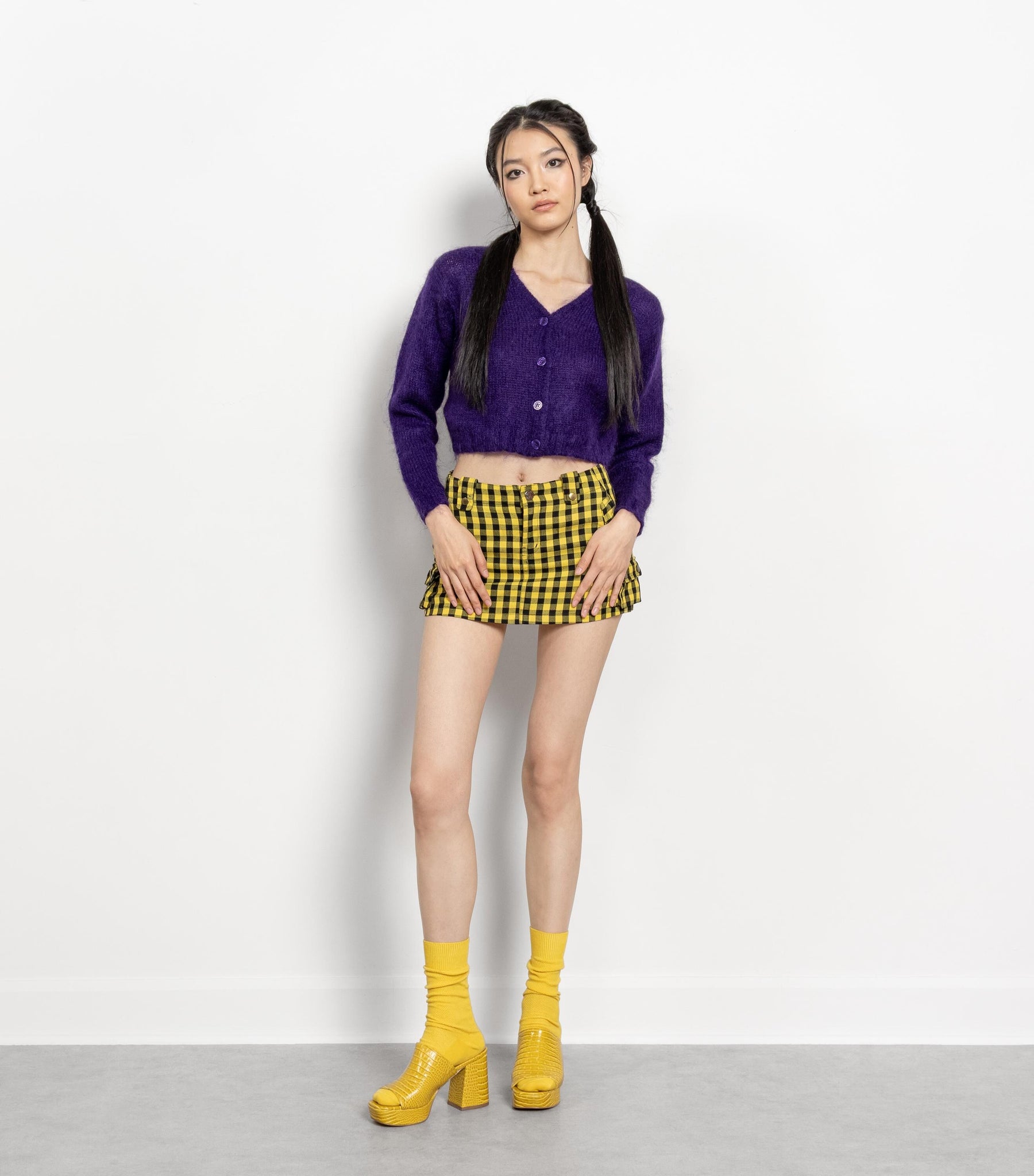 Woman wearing a purple cardigan, yellow checkered skirt, and yellow boots on a white background