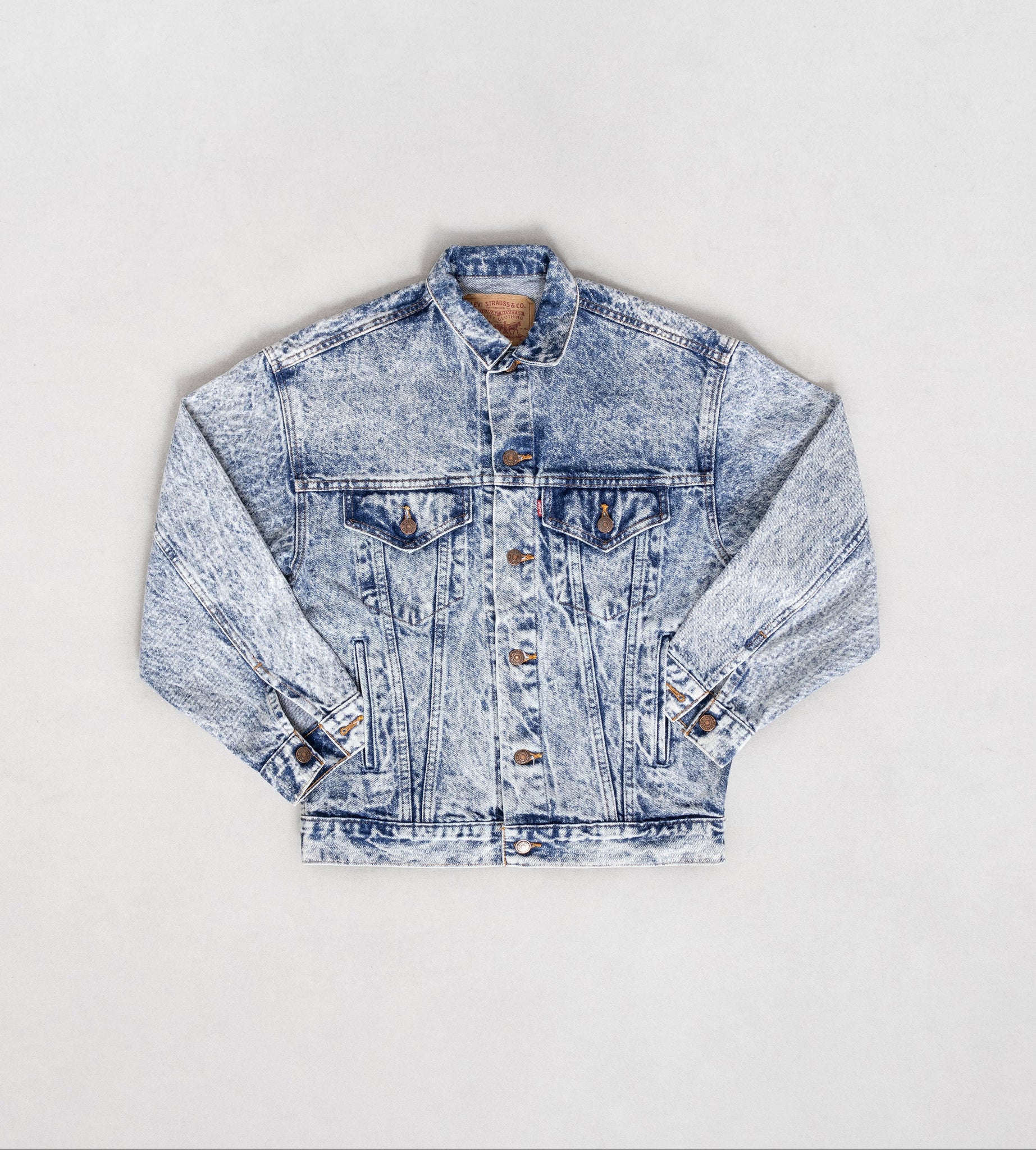 A classic Levi's acid wash light-medium blue denim jacket displayed on a plain background, with visible front breast pockets, side pockets, and interior pockets.