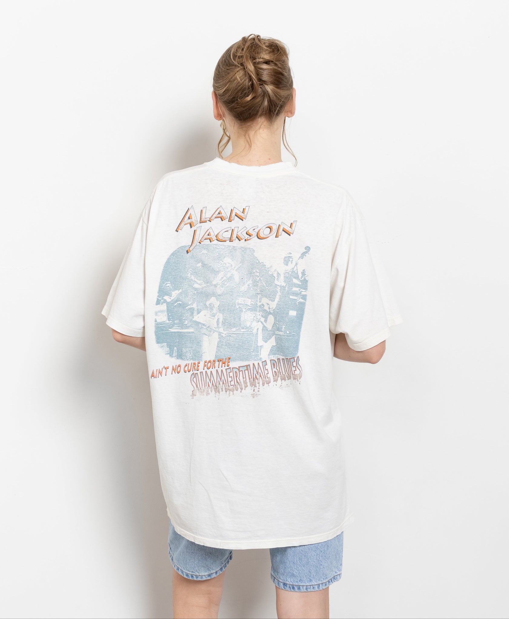 A person viewed from behind wearing a vintage white t-shirt with 'Alan Jackson Summertime Blues' text and graphics on the back.