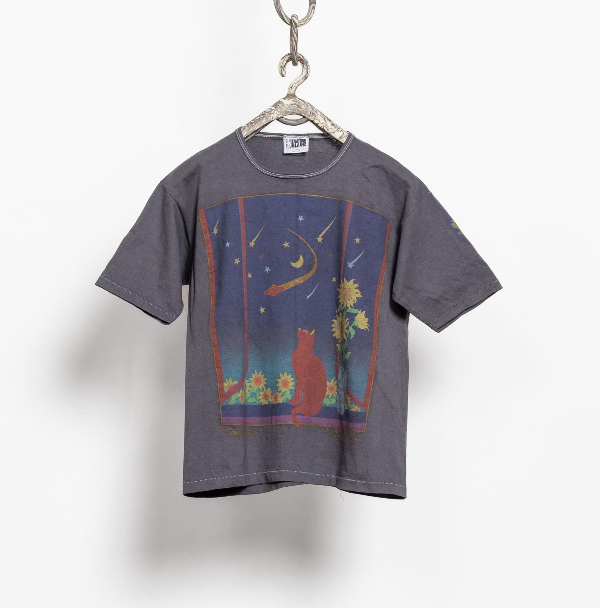 A gray over-dyed vintage 90's cotton t-shirt with a colorful front graphic featuring a cat and ufo theme, hung on a hanger against a white background.