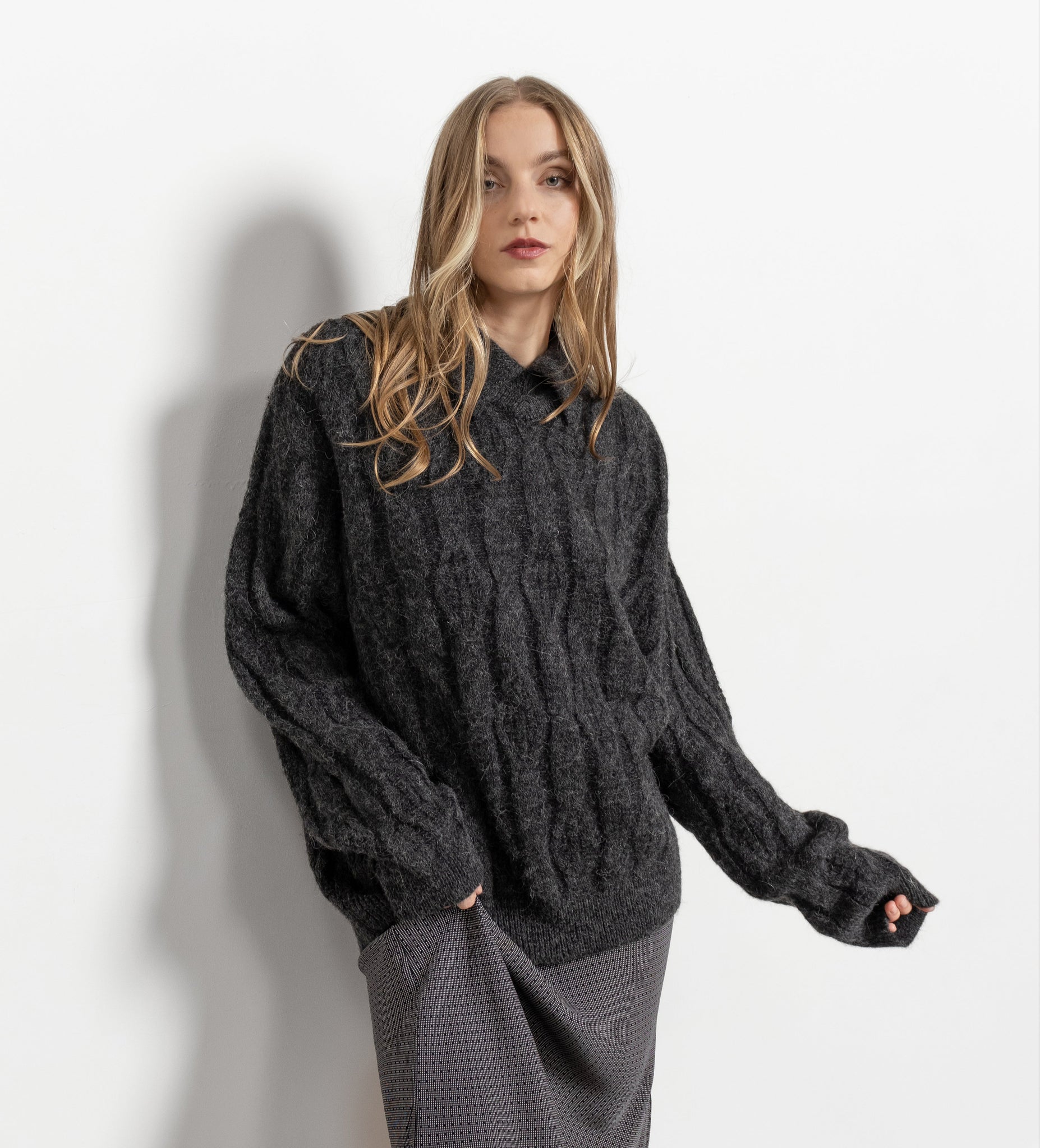 A female model wearing a vintage 90's alpaca-wool blend pullover sweater in gray, with a collared neckline, and a mid-length cut. She is also wearing a gray skirt.