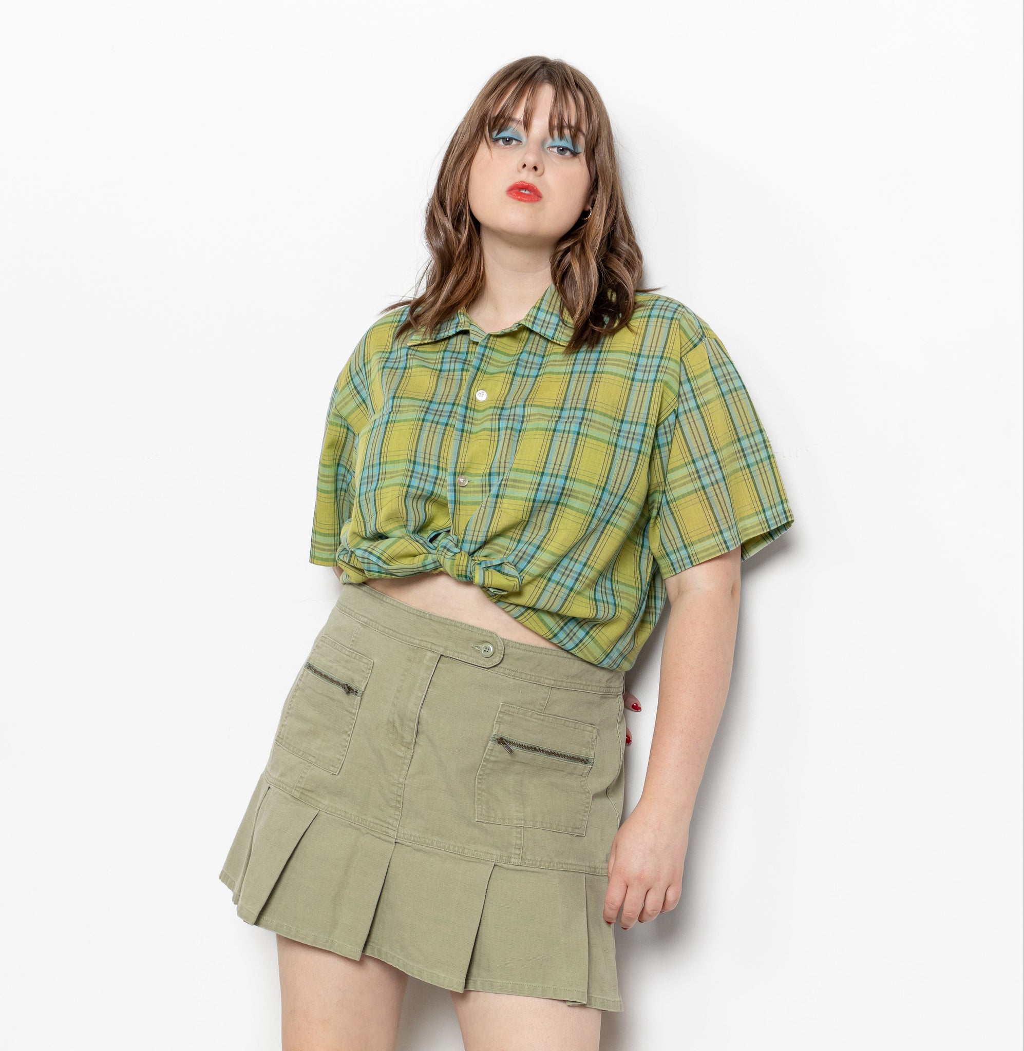 Person wearing a green plaid shirt and olive green skirt on a white background