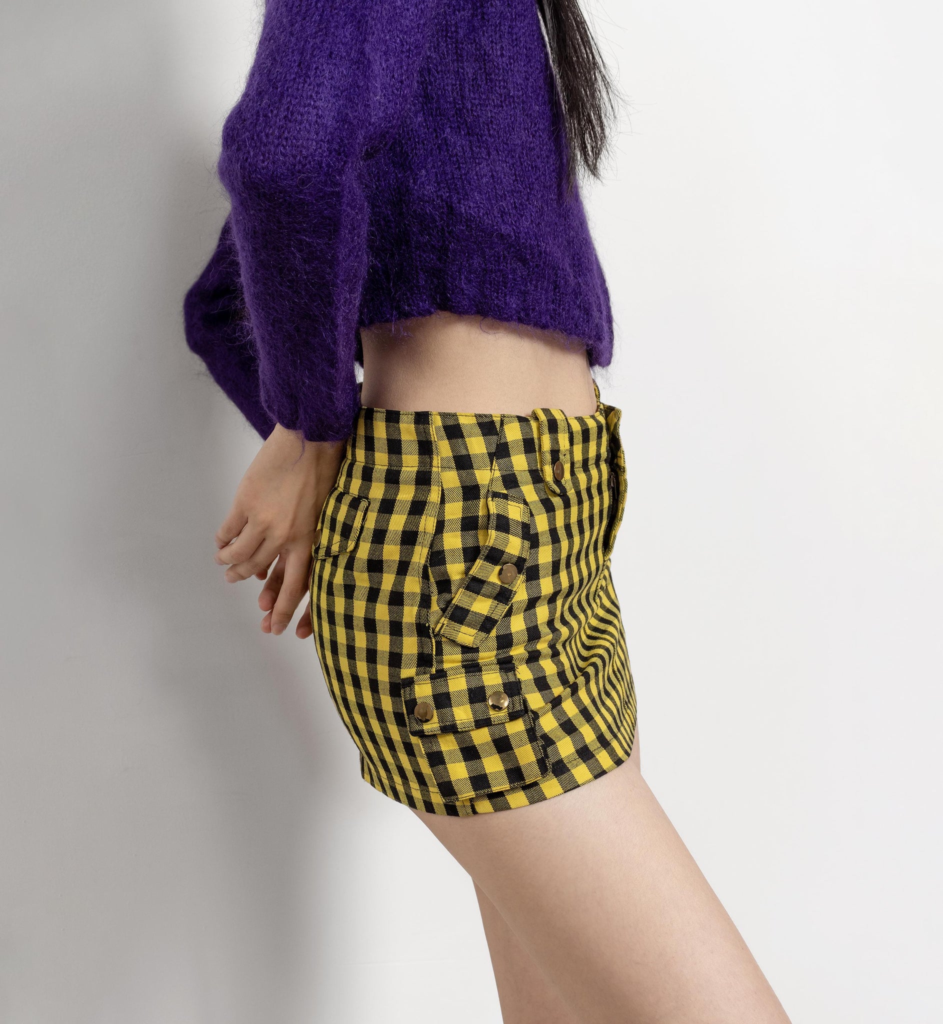Person wearing a purple sweater and yellow checkered shorts on a plain background