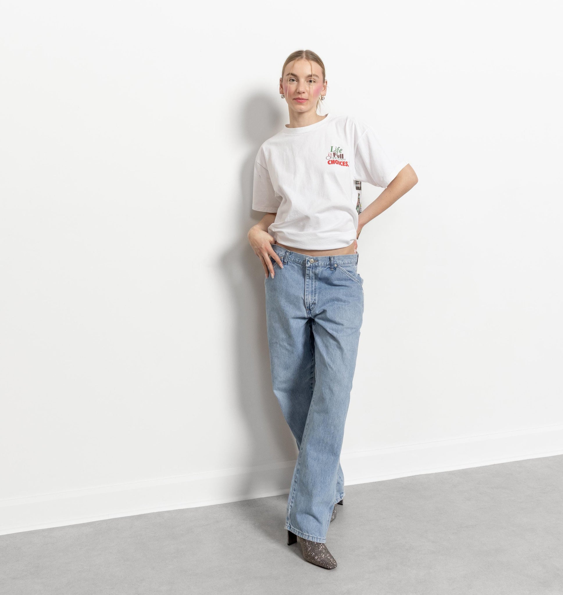 A person standing against a white background, wearing a white t-shirt and blue wide-leg carpenter jeans.