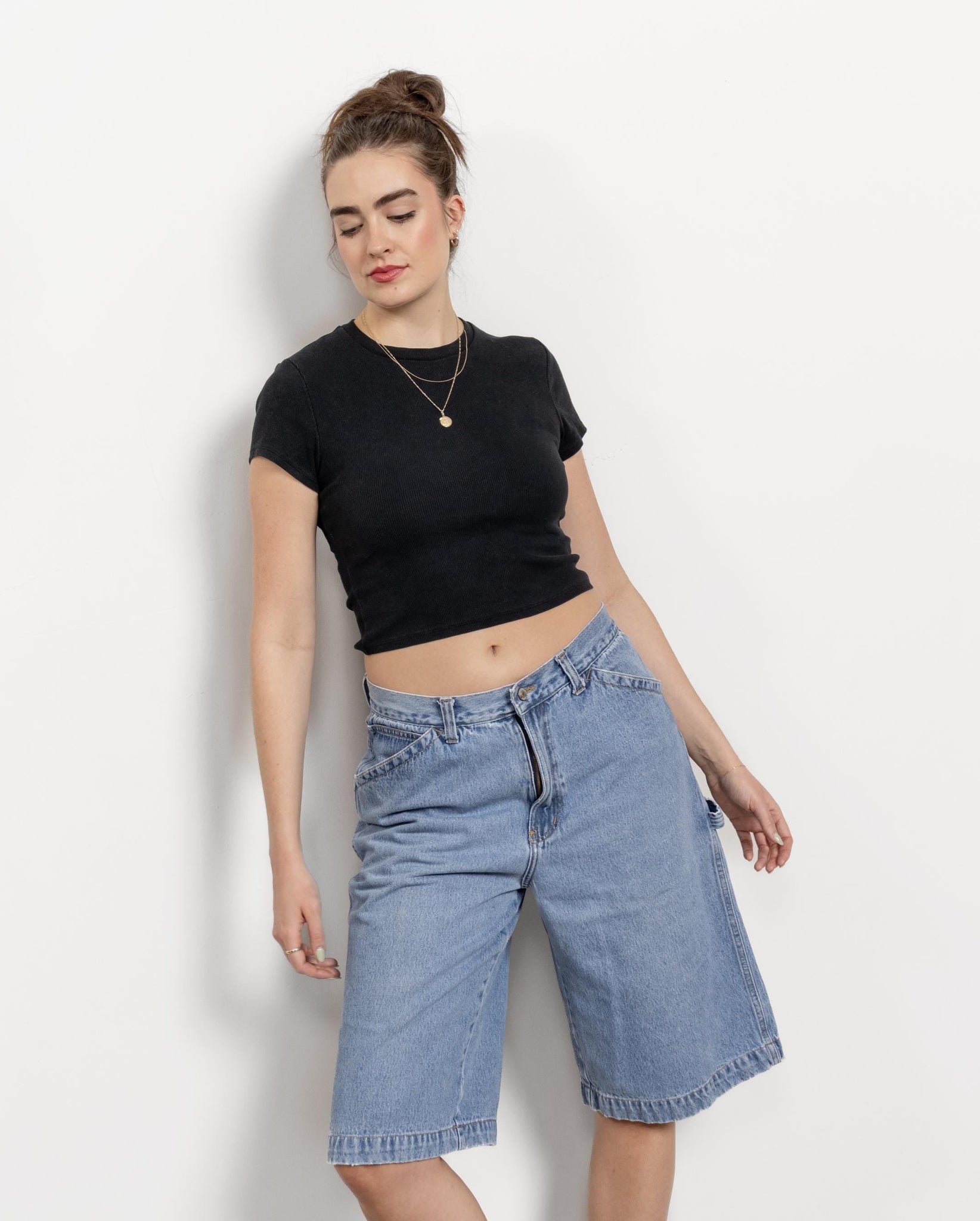 Woman wearing a black crop top and blue denim shorts against a white background