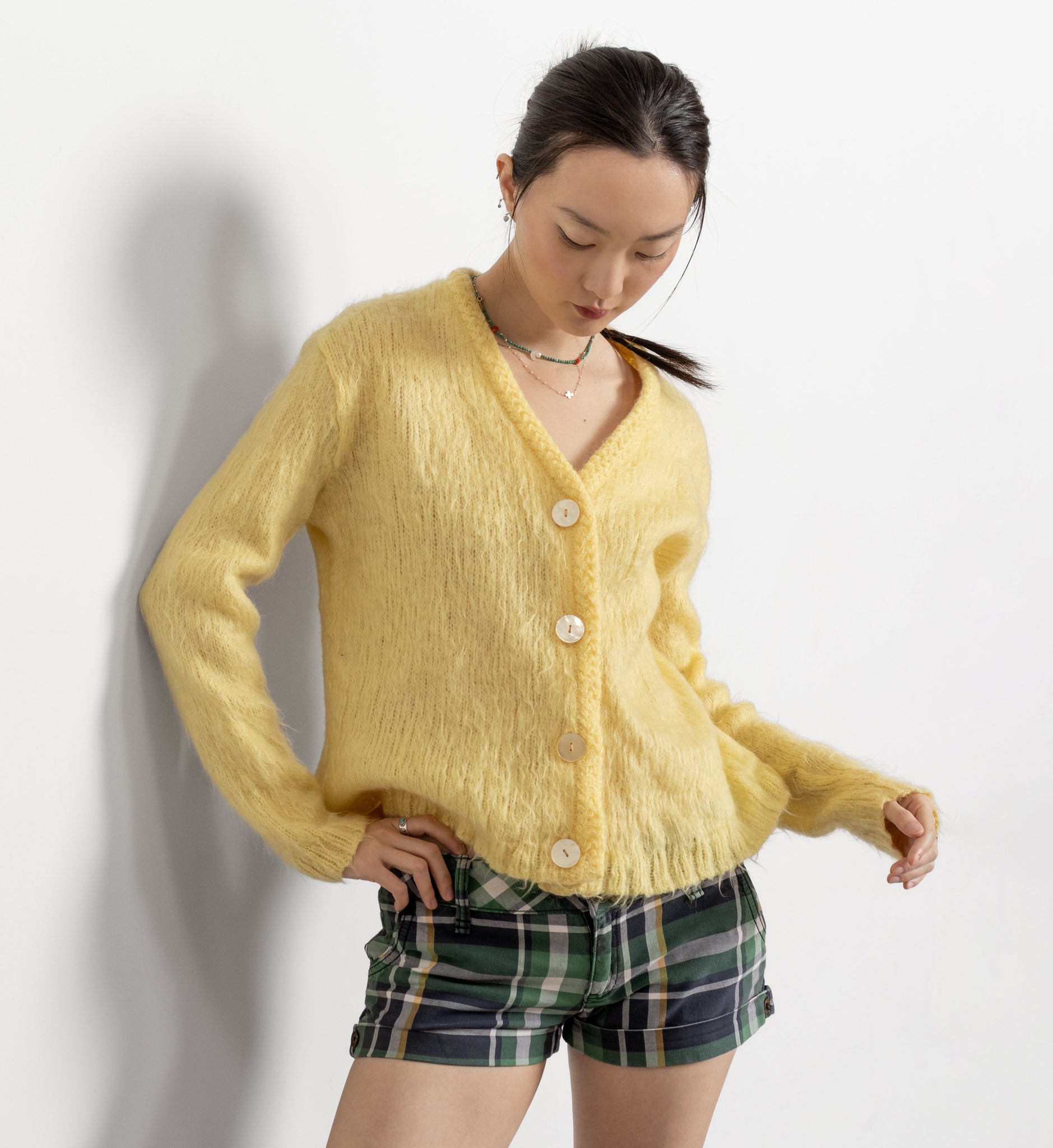 Woman wearing a yellow cardigan and plaid shorts on a white background