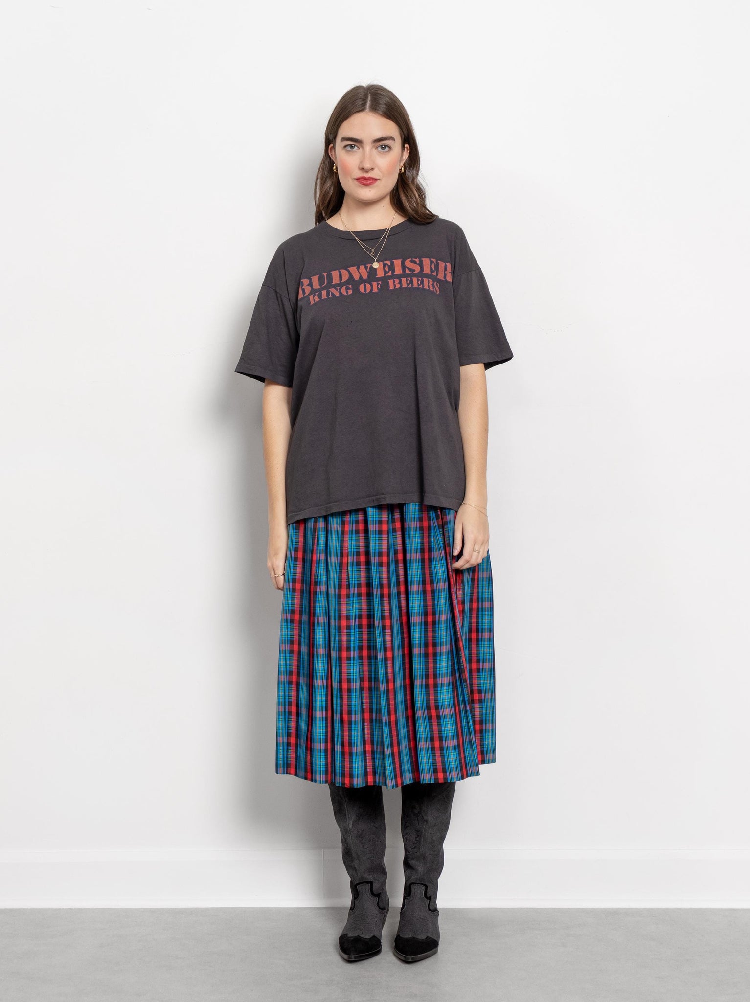 Person wearing a dark gray t-shirt with text and a plaid skirt on a white background
