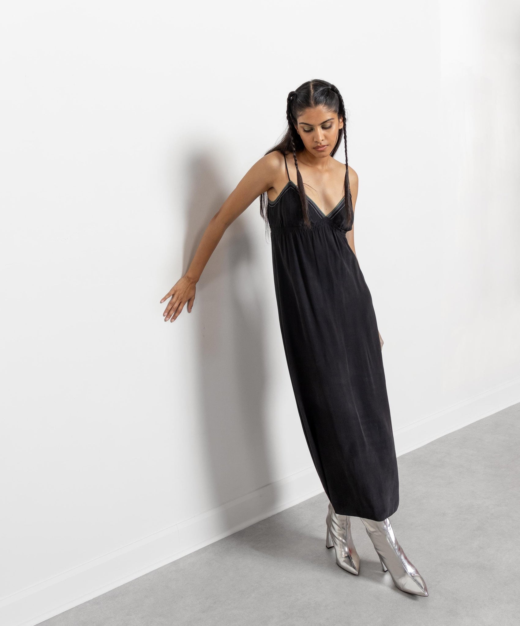 A woman modeling a vintage black maxi slip dress with spaghetti straps and a sheer mesh panel at the bodice, standing in a room with a white background.