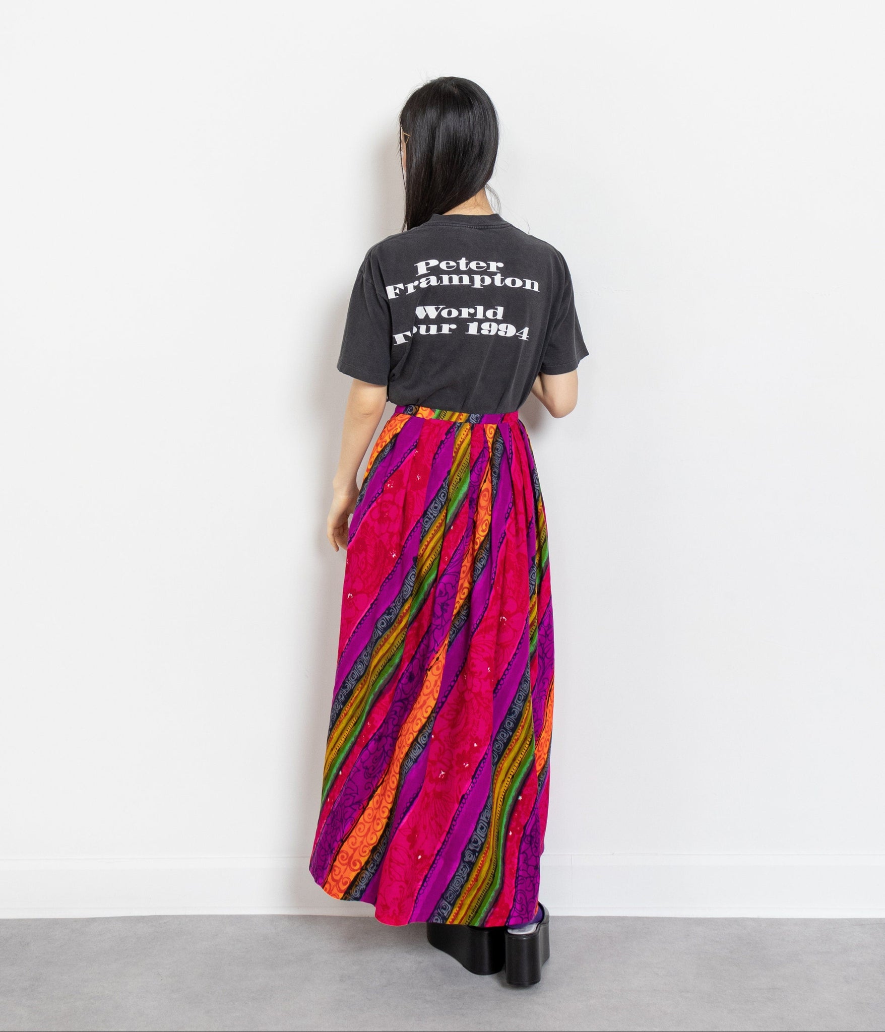 Person wearing a black t-shirt with text and a colorful striped dress against a white background