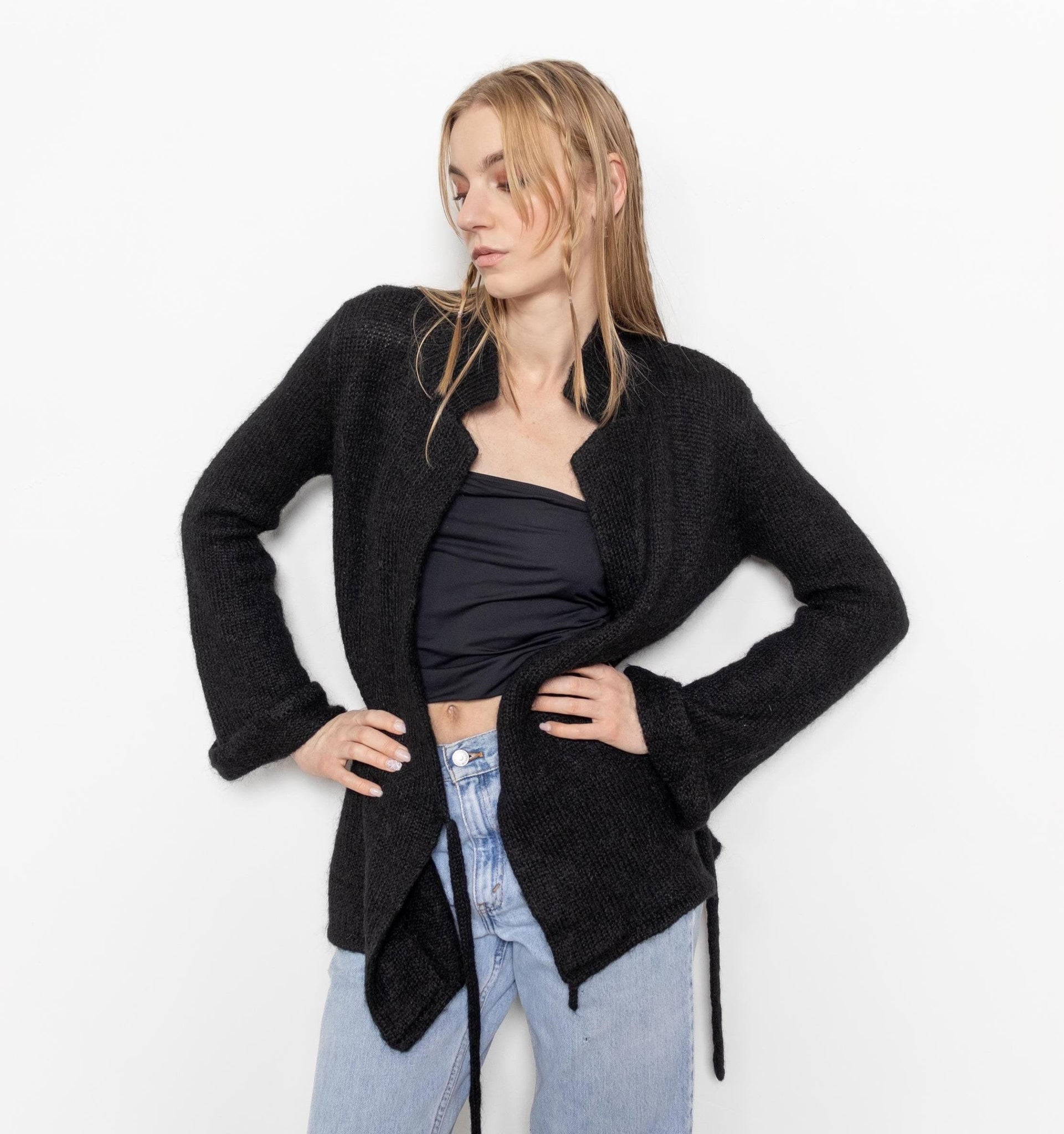 Woman wearing a black cardigan over a black top and light blue jeans on a white background