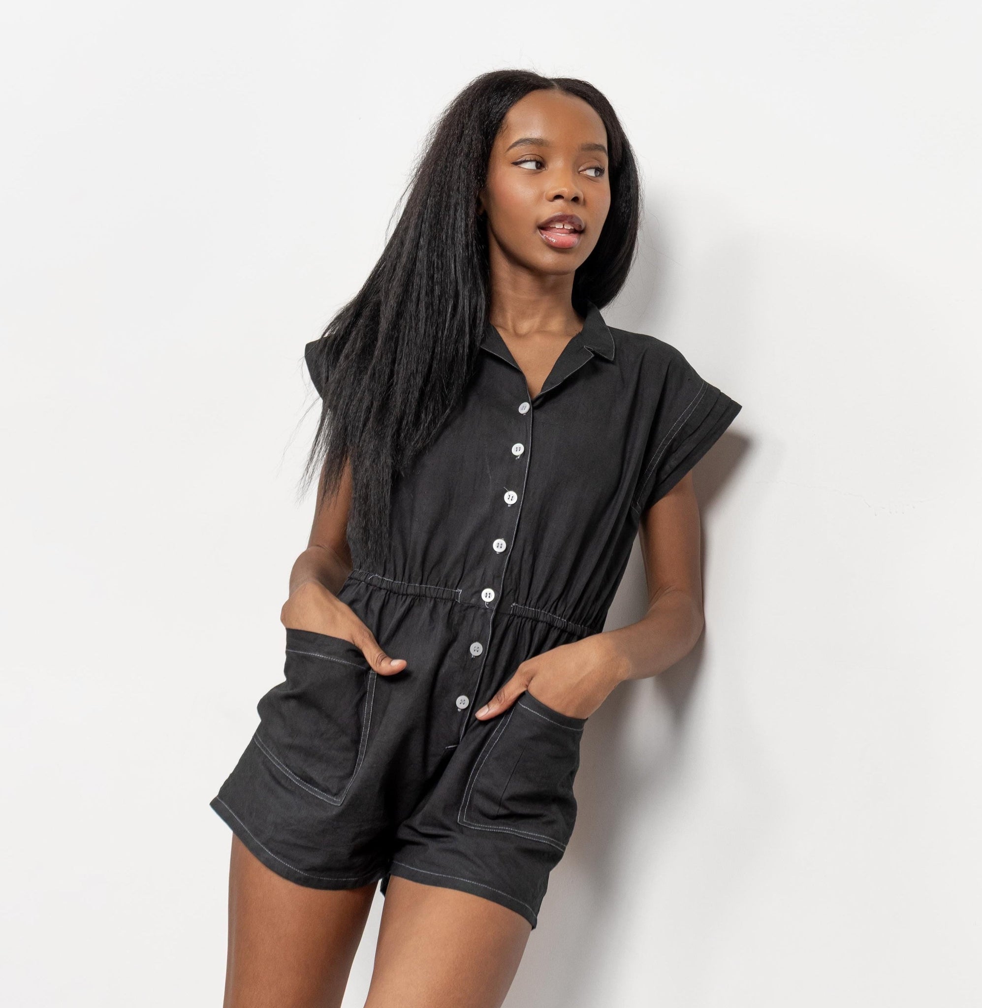 Woman wearing a black romper with white buttons against a light background