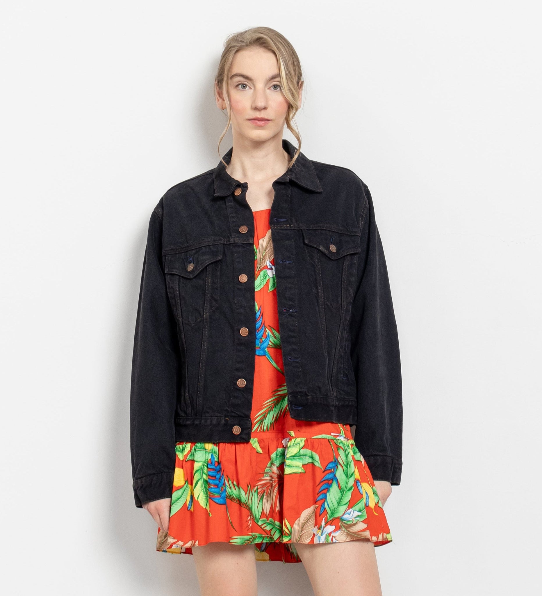 A person wearing a vintage black denim jacket with a tropical print dress.
