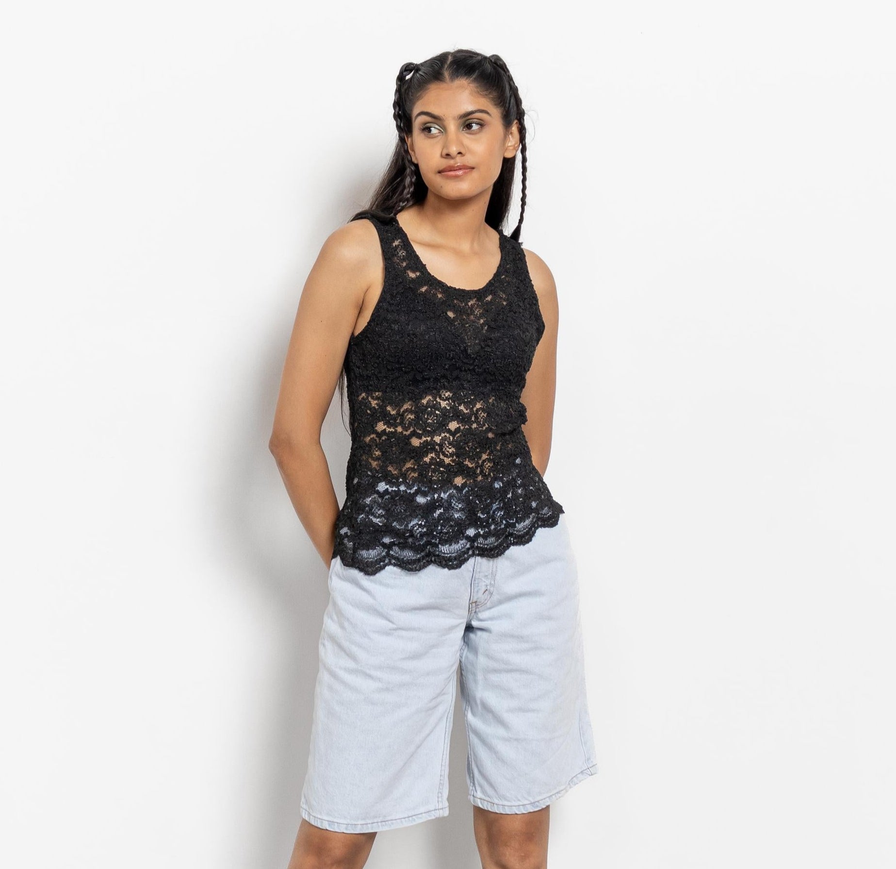 Woman wearing a black lace top, white shorts, and black knee-high boots on a white background