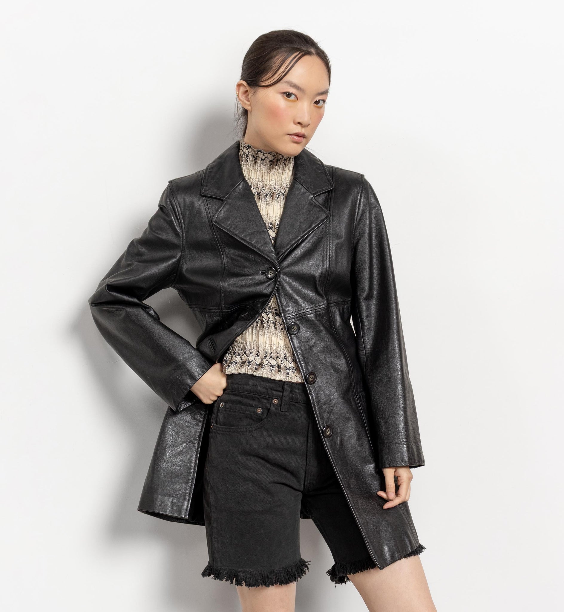 Person wearing a black leather coat and black shorts on a white background