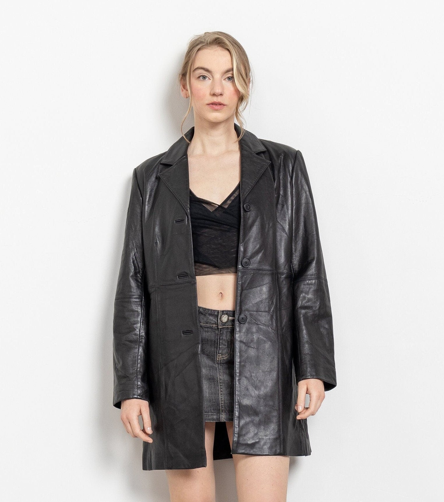 Person wearing a black leather coat, black top, and black boots on a white background