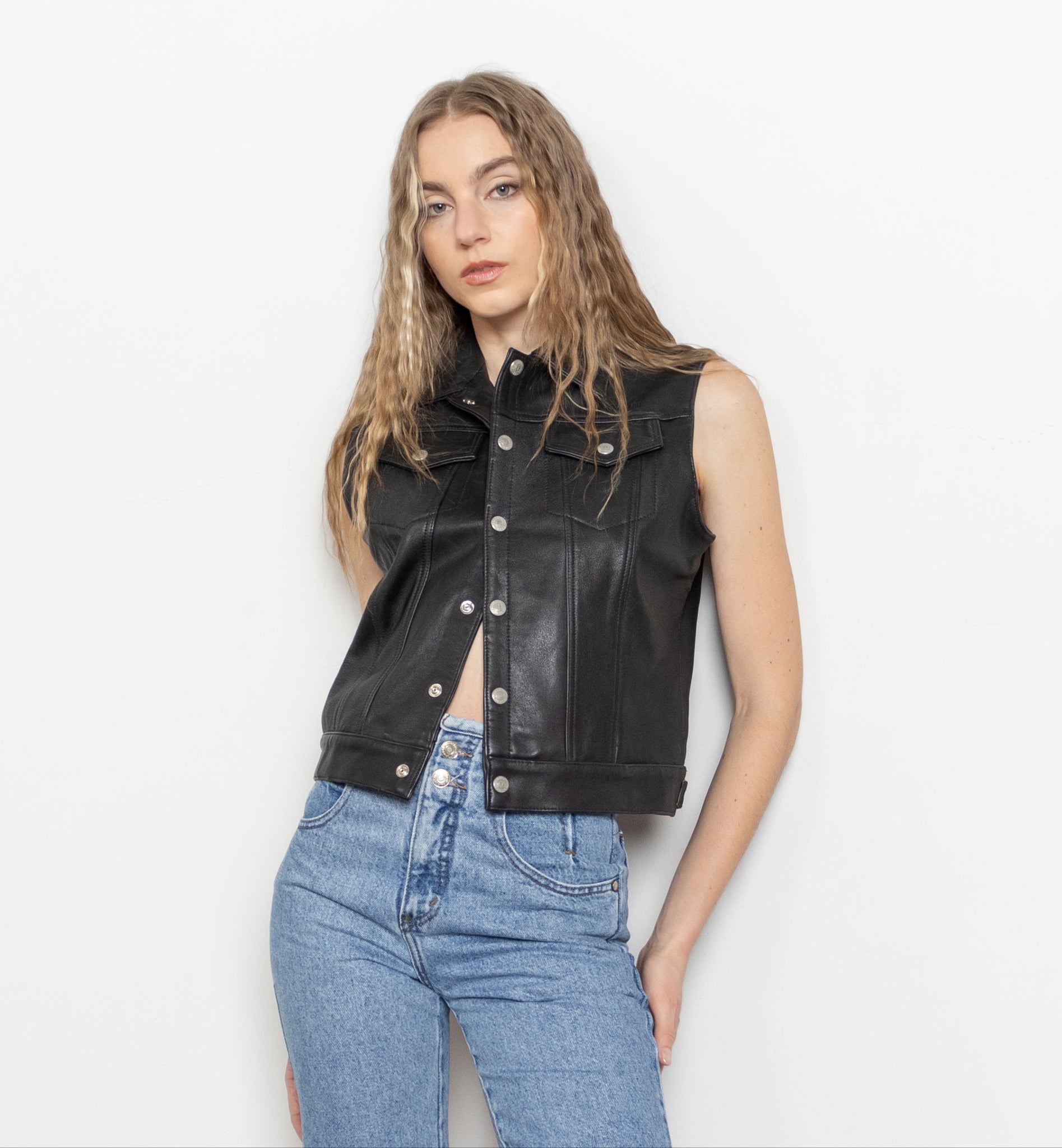 Woman wearing a black leather vest, blue denim shorts, and black knee-high boots against a white background