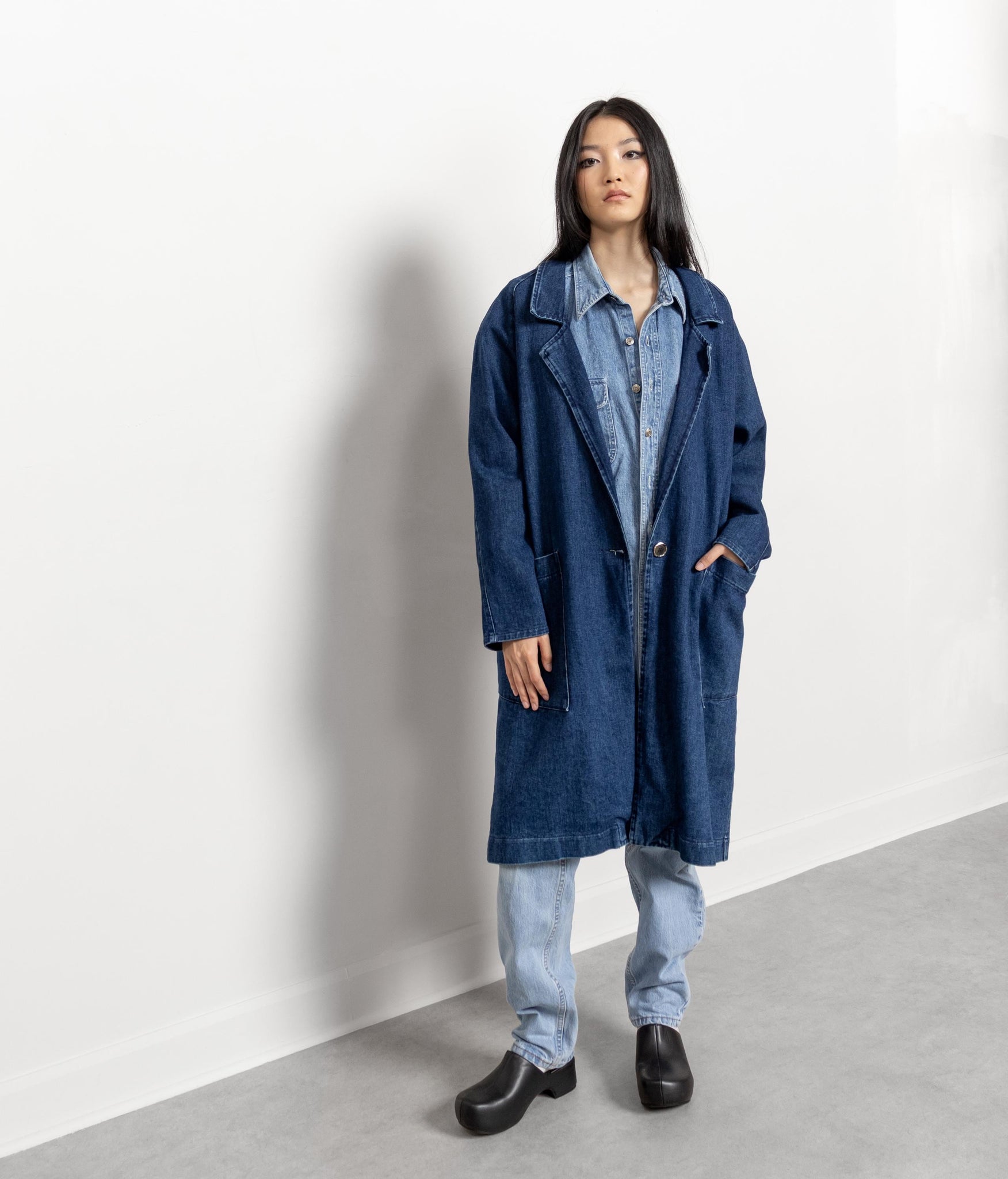 Person wearing a blue denim coat over a denim shirt against a white background