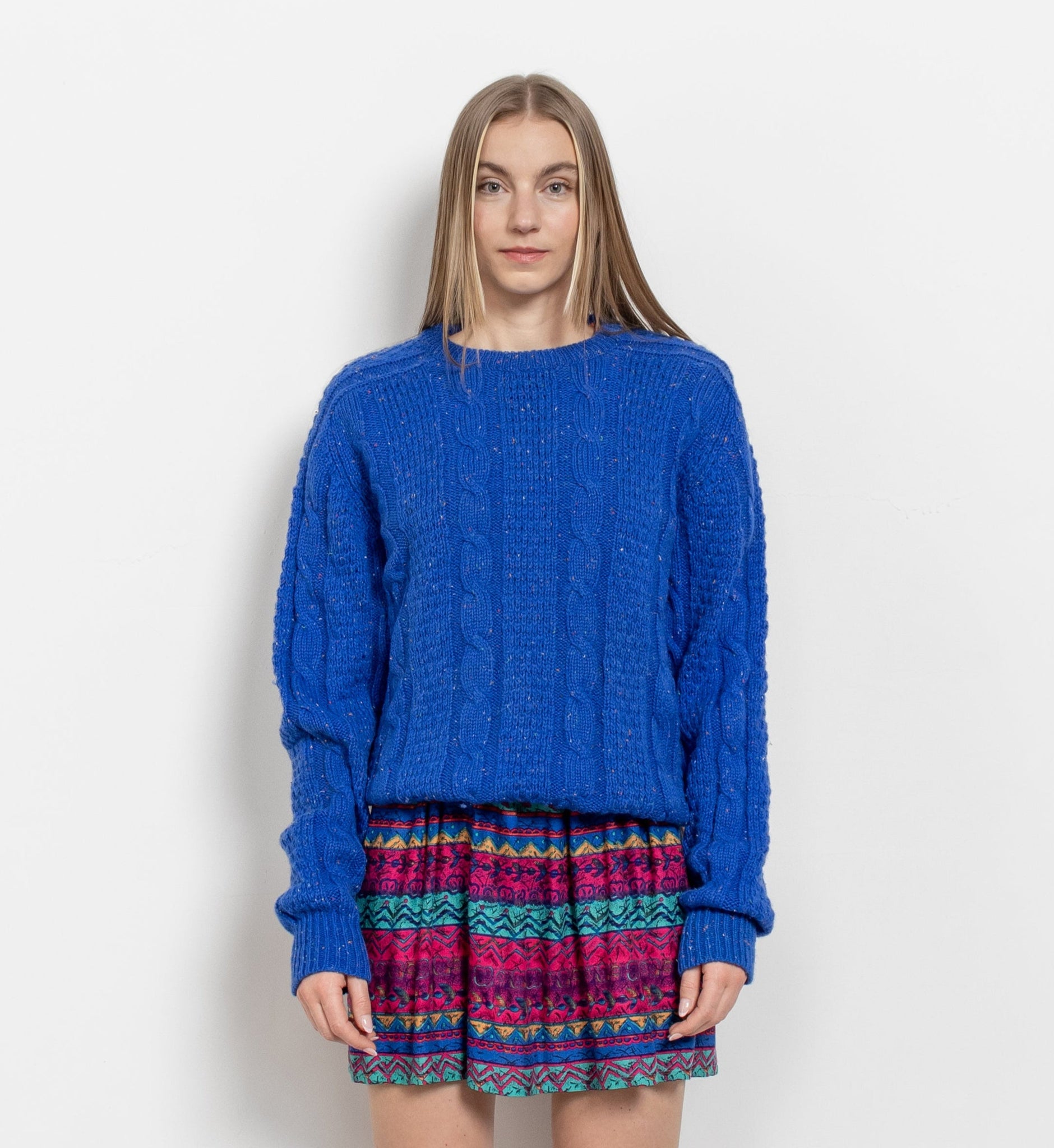 Woman wearing a blue sweater and patterned skirt on a white background