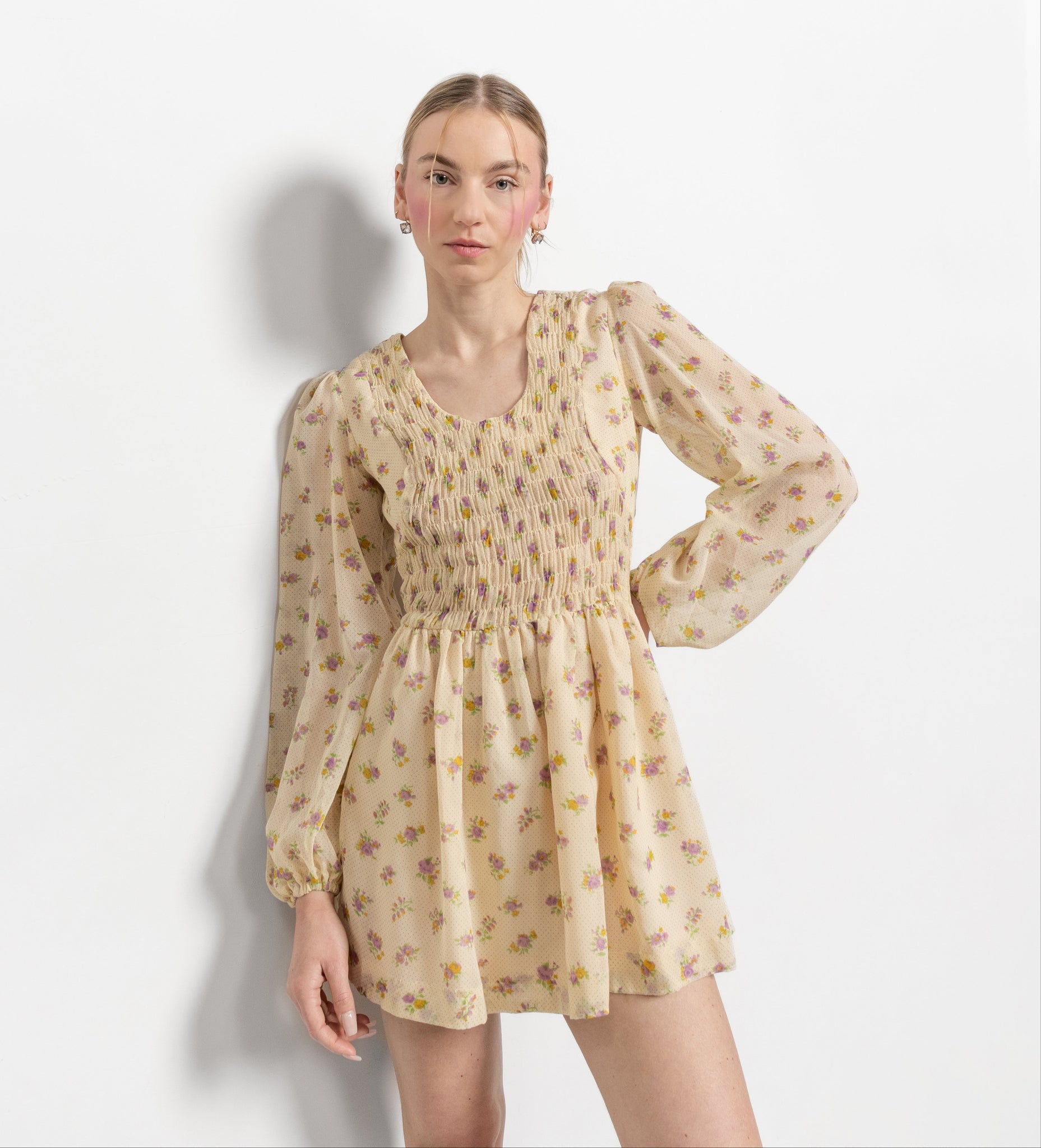A model wearing a vintage 70's pale yellow mini dress with a floral pattern, scoop neckline, and three-quarter length puffy sleeves.