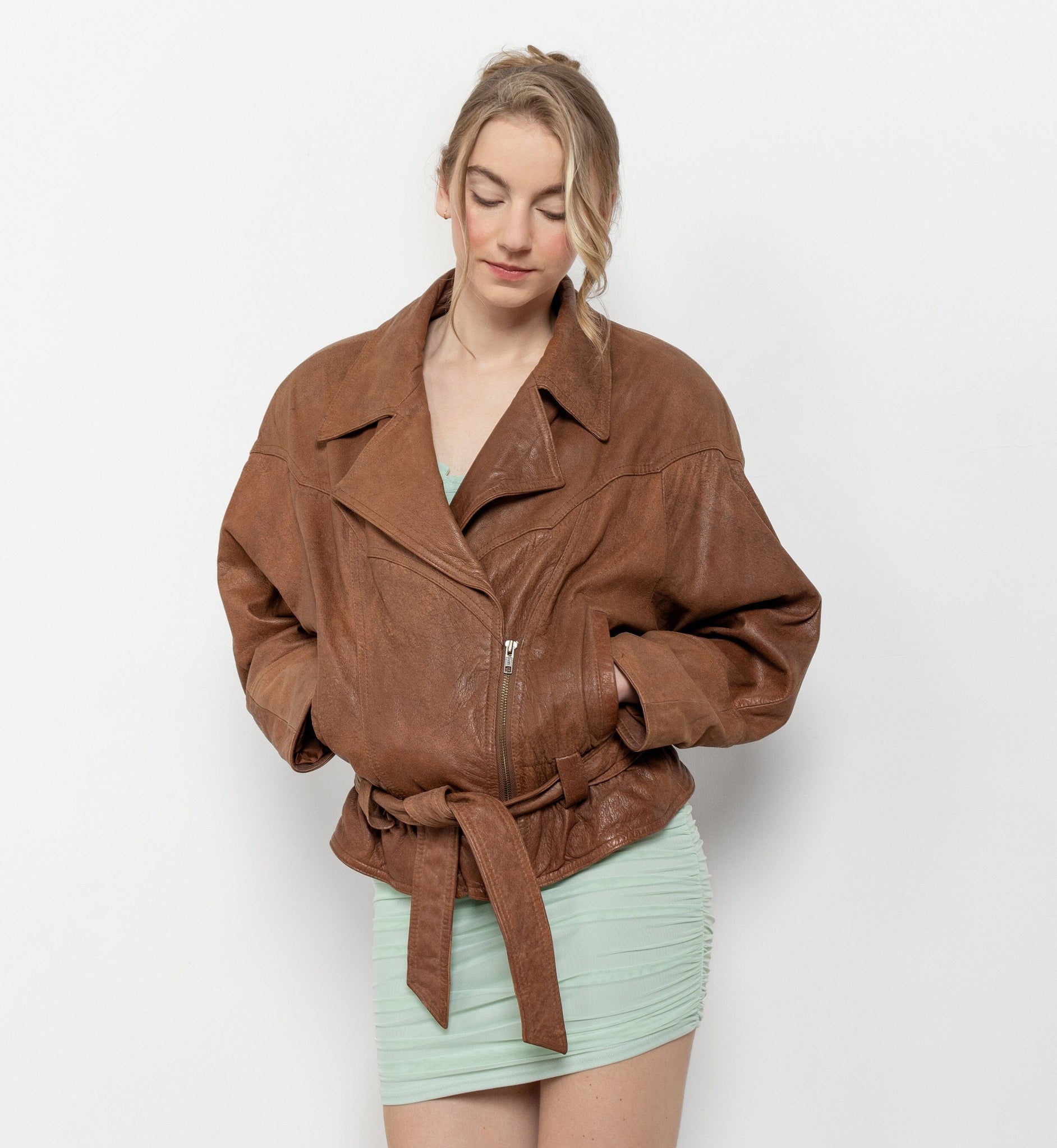 Woman wearing a brown leather jacket and light green skirt on a white background