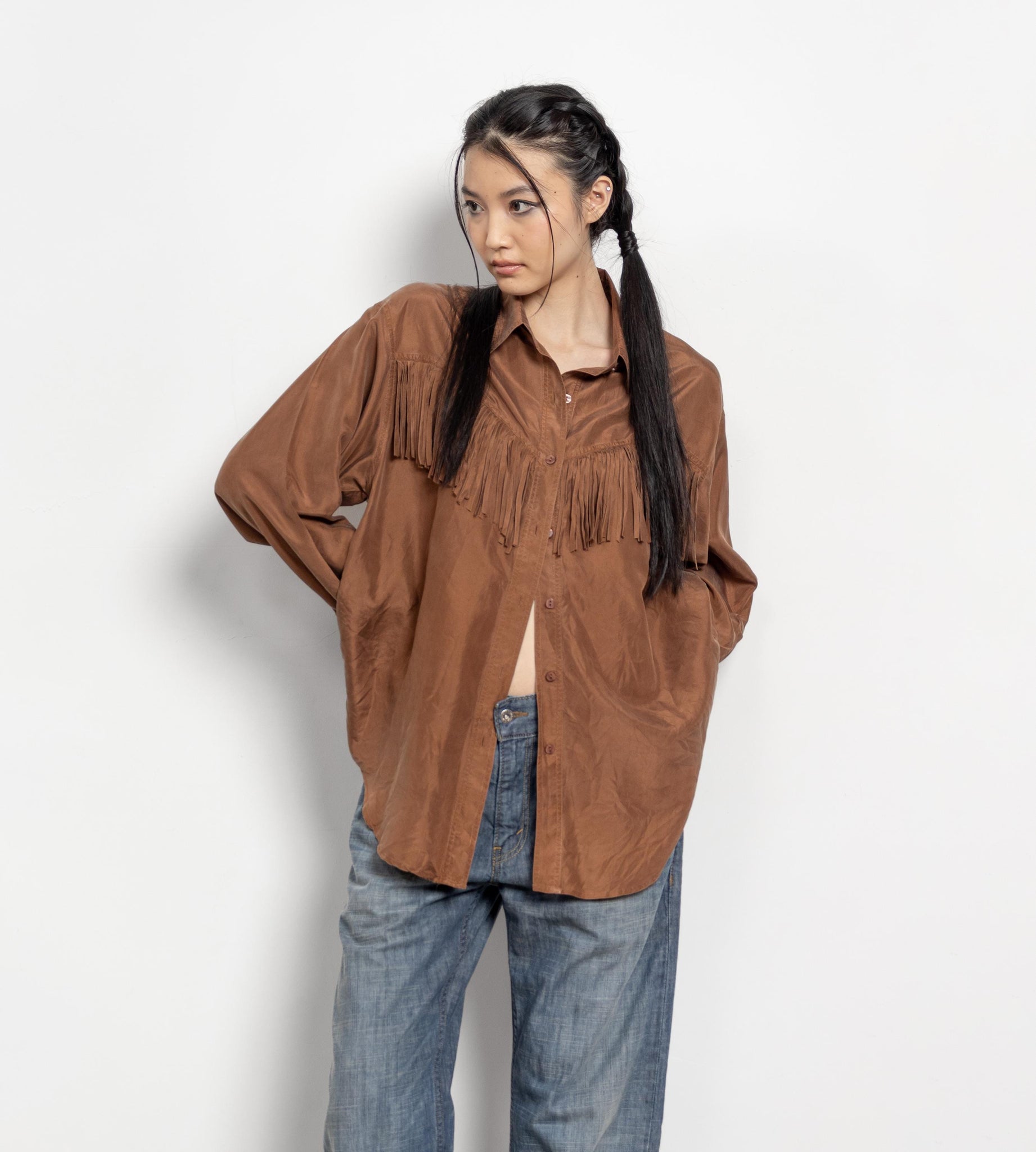 Person wearing a brown fringed shirt and blue jeans on a white background