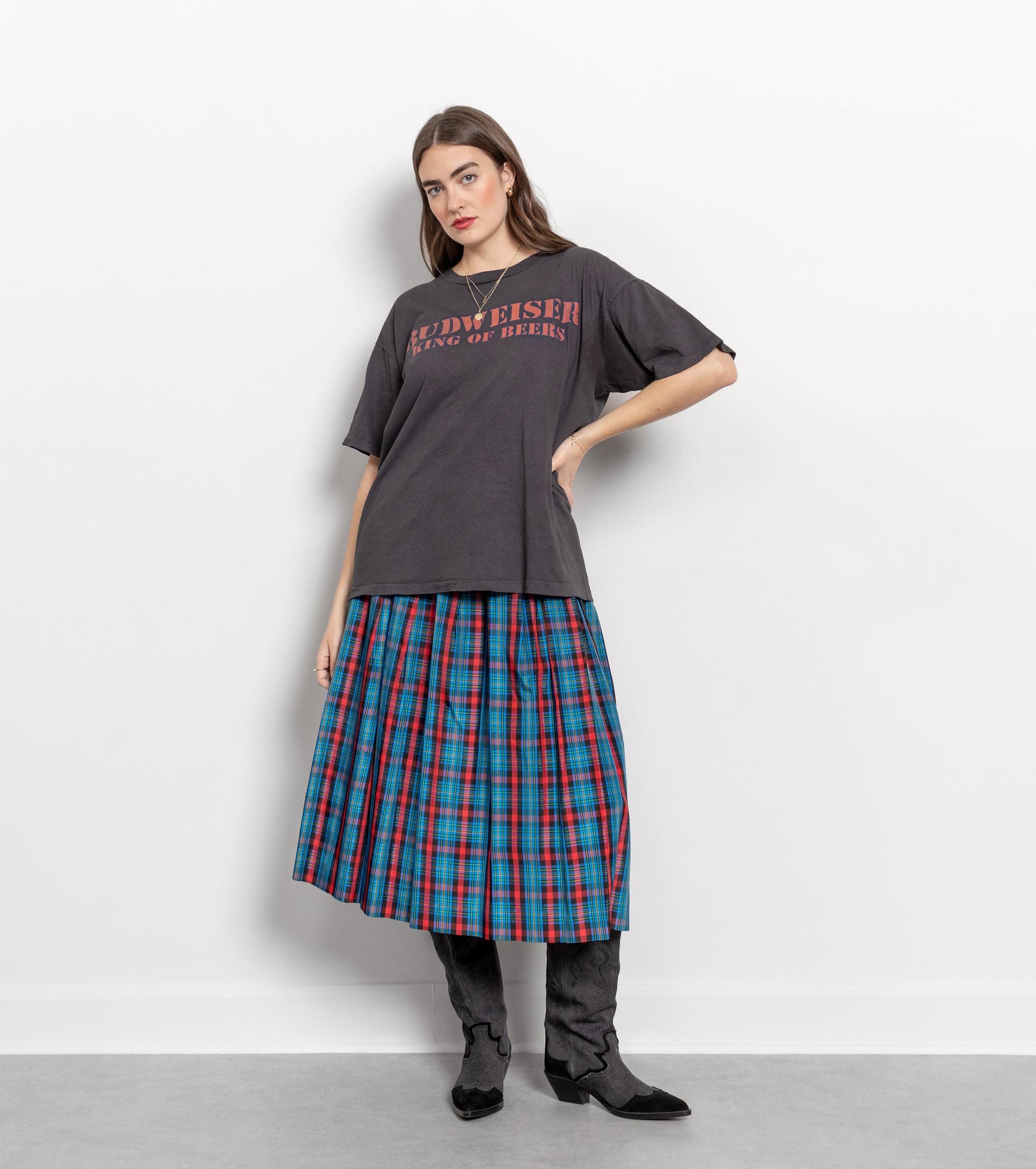 Woman wearing a dark gray oversized t-shirt with text and a plaid skirt on a white background