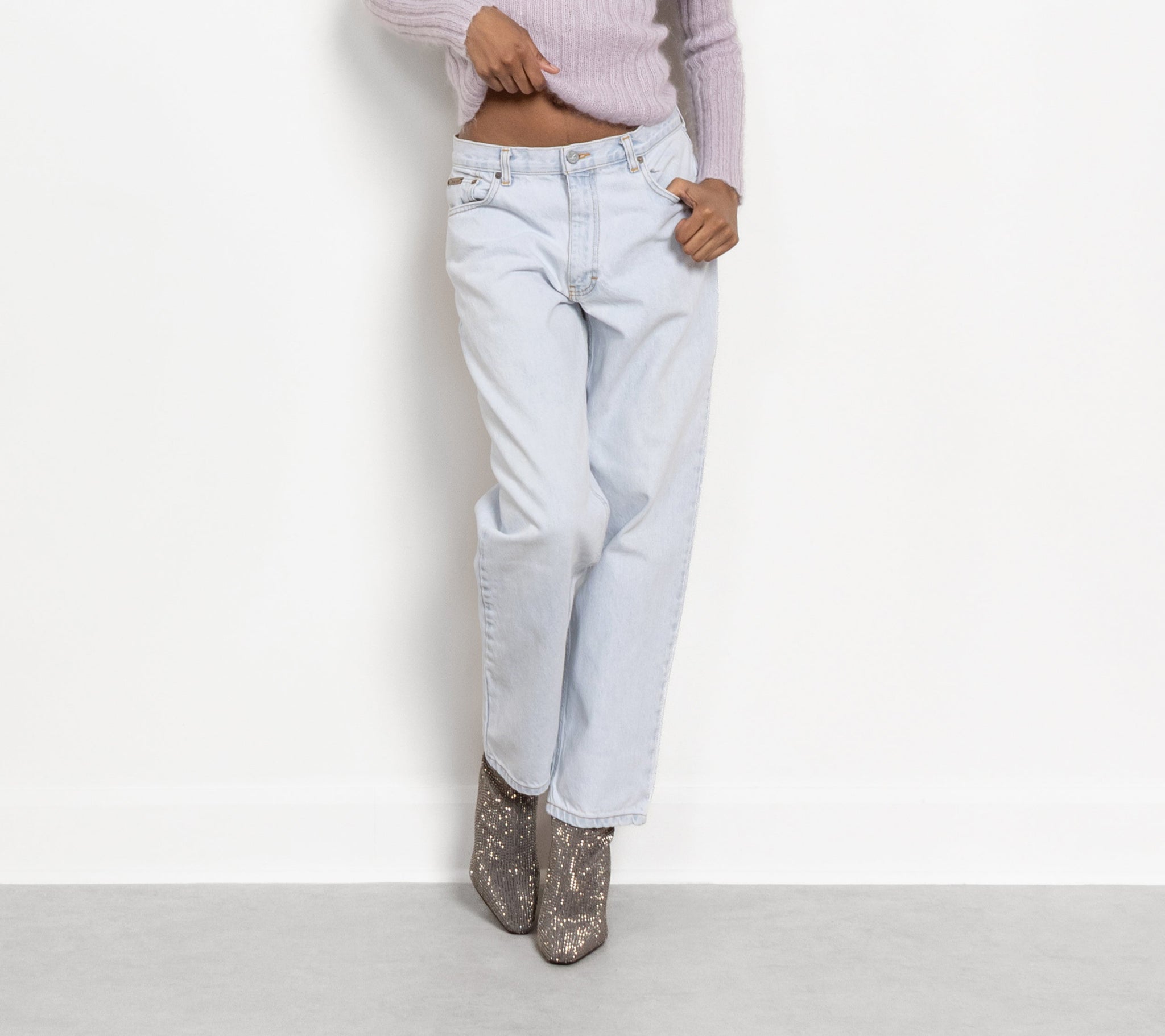 Woman wearing a light purple off-shoulder top and light blue jeans against a white background