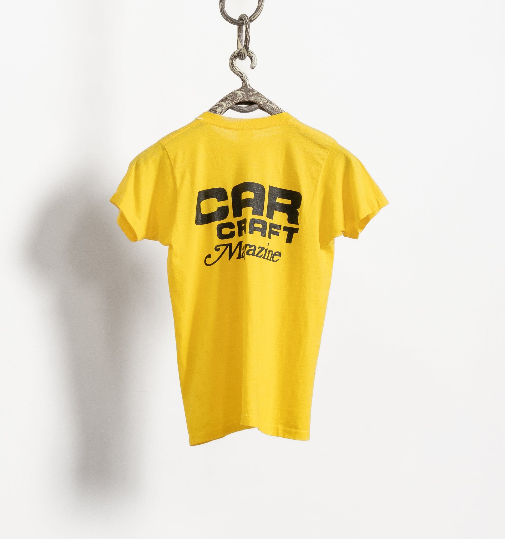 Yellow t-shirt with 'Car Craft Magazine' text on a hanger against a white background