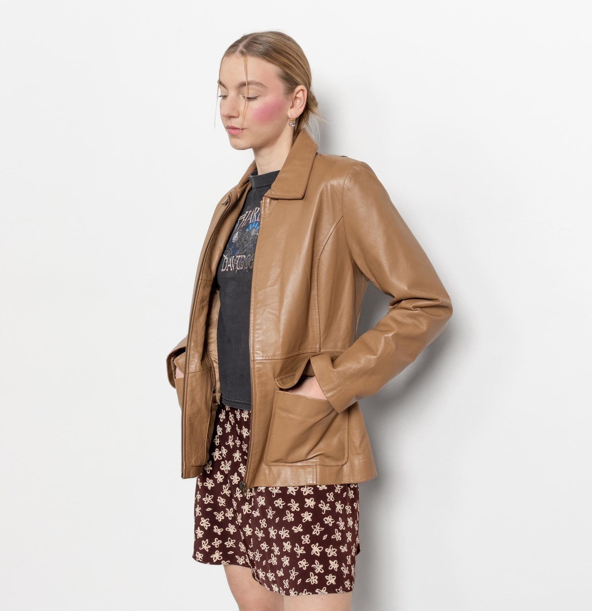 Woman wearing a brown leather jacket and patterned skirt against a white background