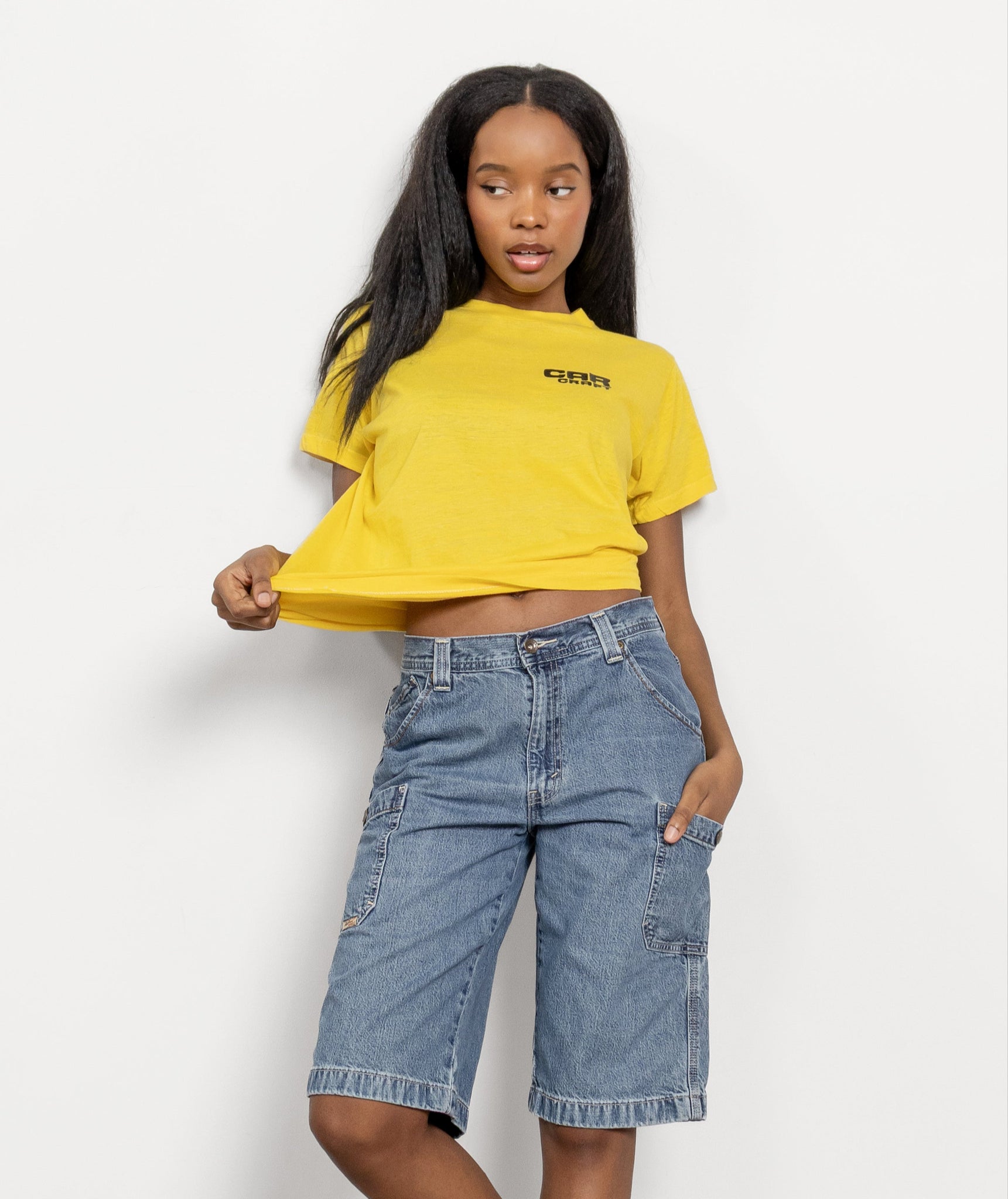 Person wearing a yellow crop top and blue denim shorts on a white background