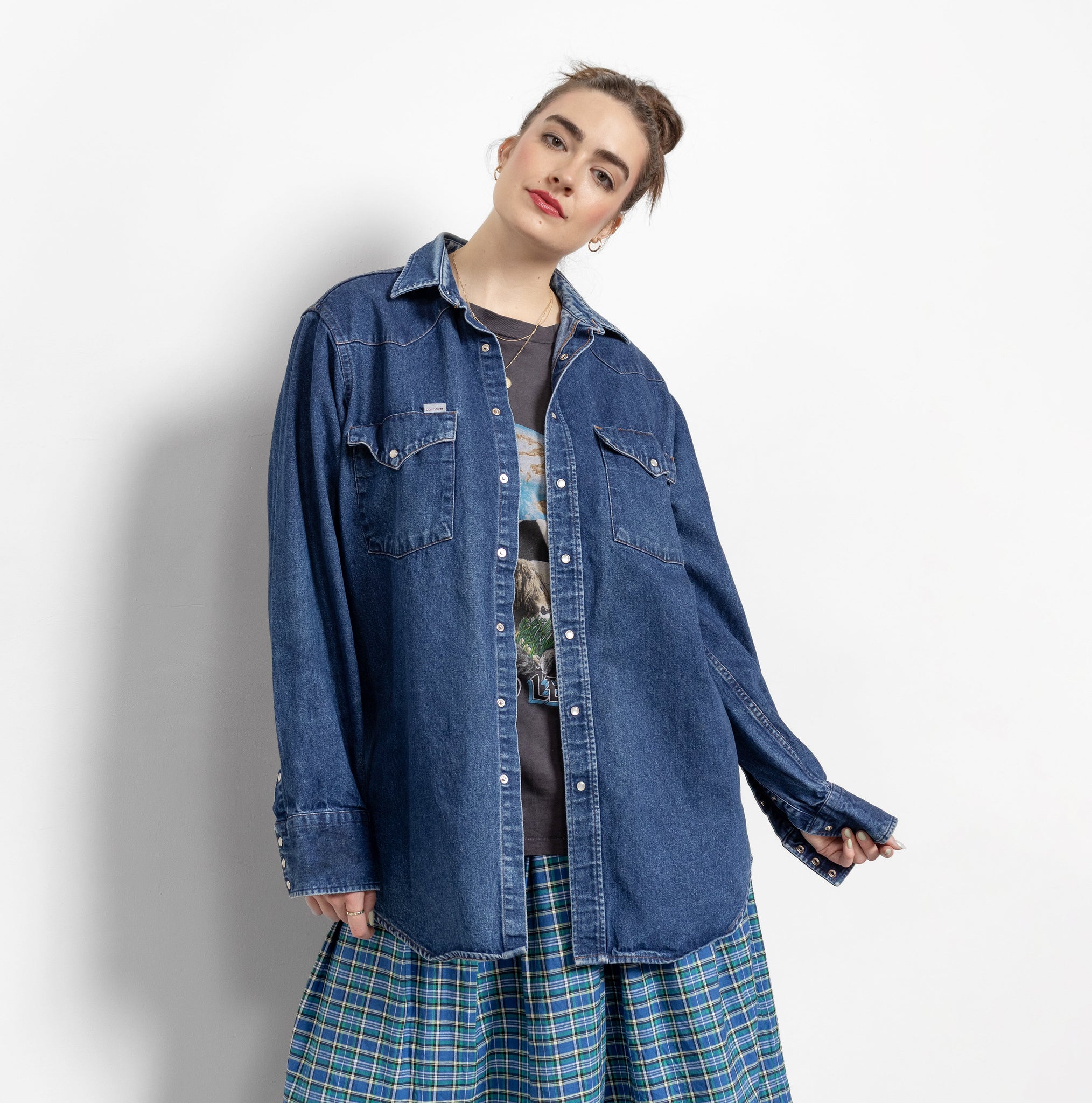 Person wearing a blue denim jacket over a plaid skirt on a white background