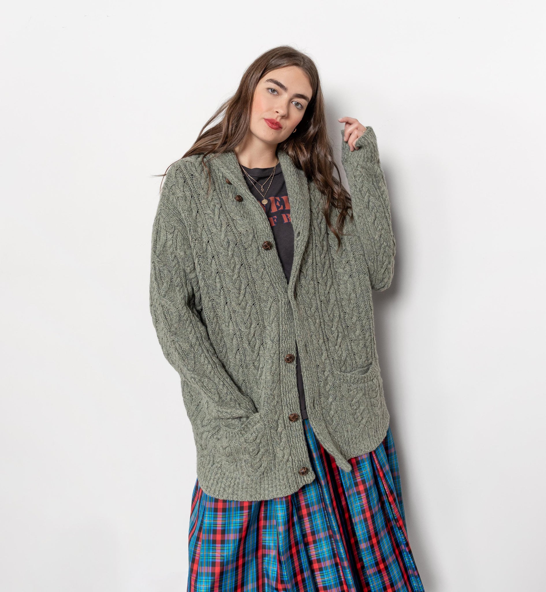 Woman wearing a green cardigan over a plaid skirt on a white background
