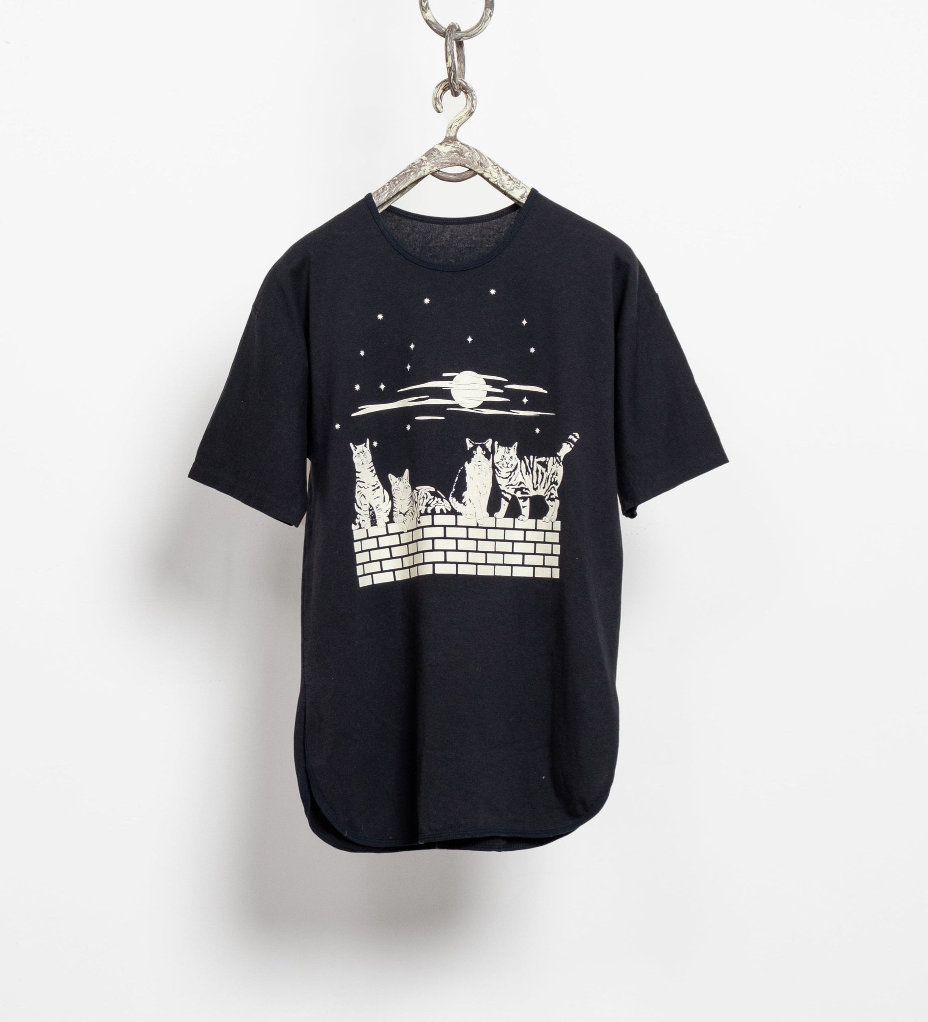Black t-shirt with a graphic design of cats on a wall and moon, hanging on a white background.
